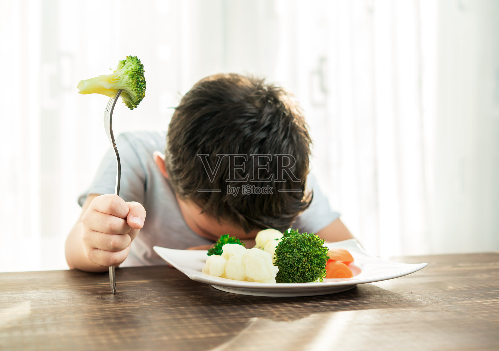 孩子对不得不吃蔬菜很不高兴。照片摄影图片