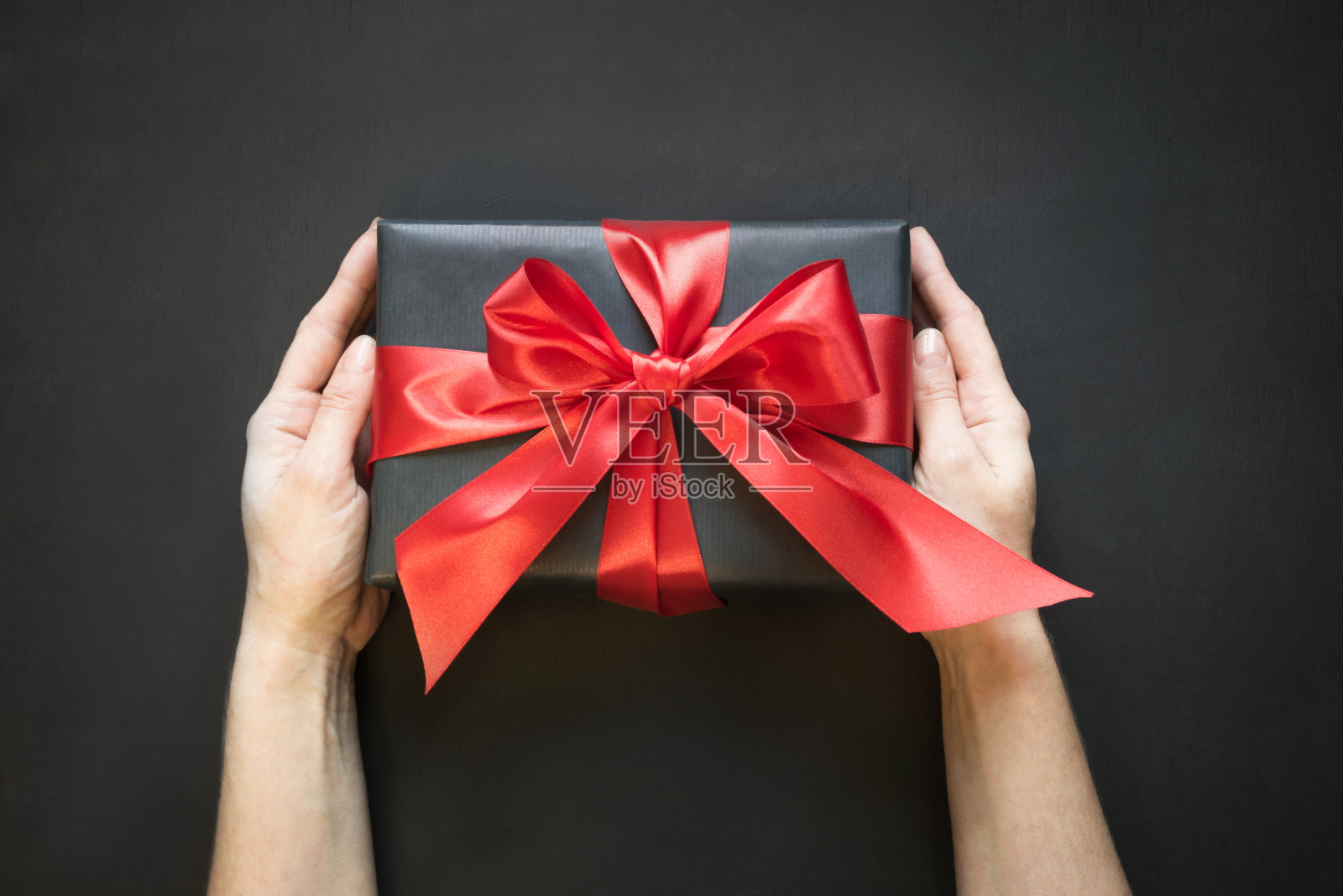 礼盒用黑色纸包着，黑色表面，女性手拿红色丝带。照片摄影图片