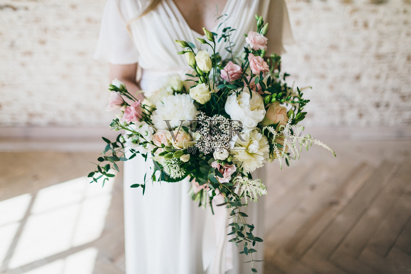 美丽的白色和粉红色的鲜花捧在迷人的新娘手中，穿着白色的裙子。艺术作品照片摄影图片
