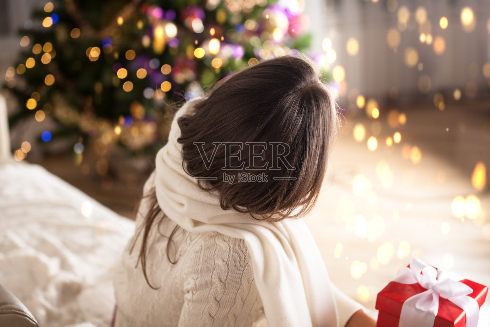拿着礼盒的女人站在圣诞树旁。照片摄影图片