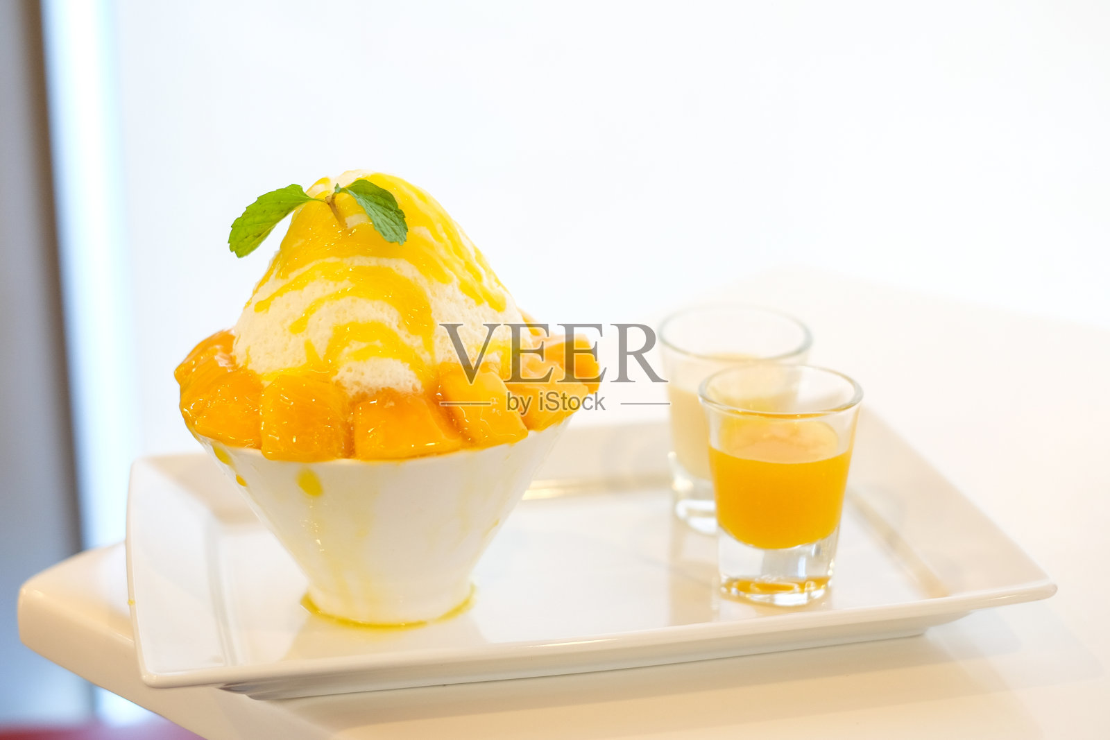 芒果冰淇淋(日本刨冰口味的芒果冰淇淋)盛在白色的碗里，配上黄色的芒果酱和白色的牛奶，口感甜美。照片摄影图片