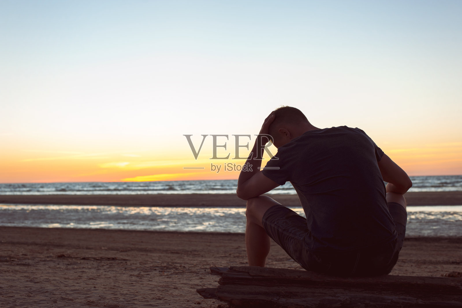 被看不见的烦恼所累。一个悲伤孤独的男人坐在海滩上照片摄影图片