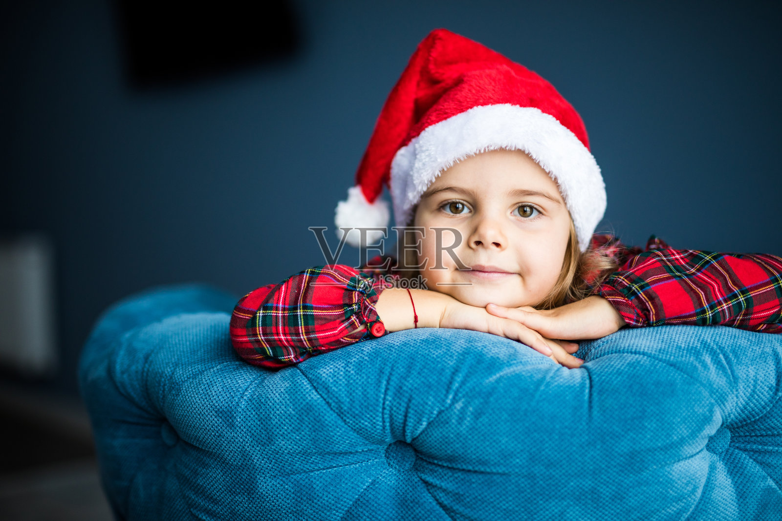 快乐的漂亮小女孩的肖像戴着圣诞老人的帽子在椅子上等待圣诞老人的礼物微笑着在家照片摄影图片