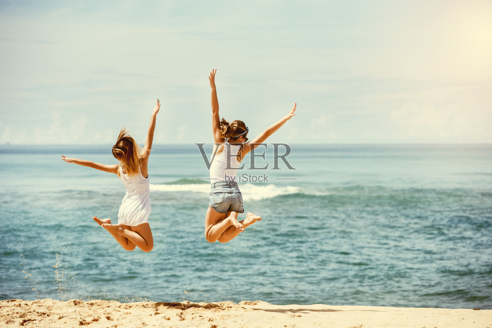 两个快乐的女孩在阳光沙滩上跳跃照片摄影图片