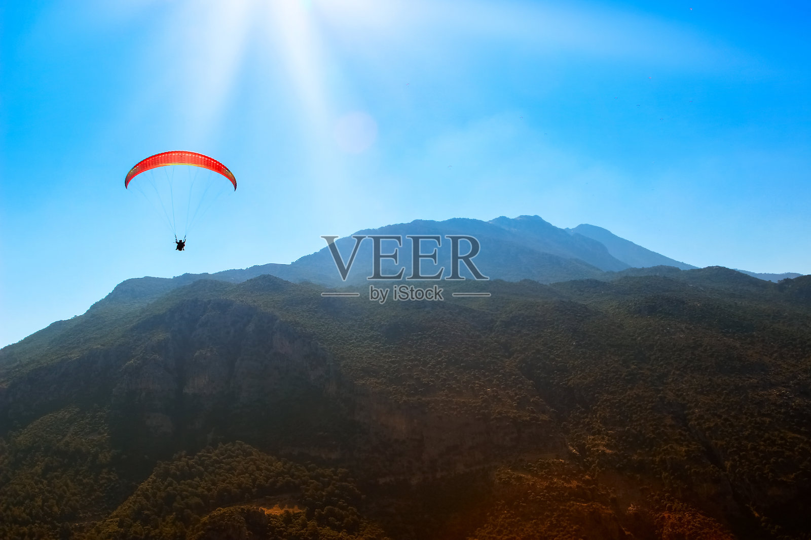 红色的降落伞在山上的天空中。跳伞运动。照片摄影图片