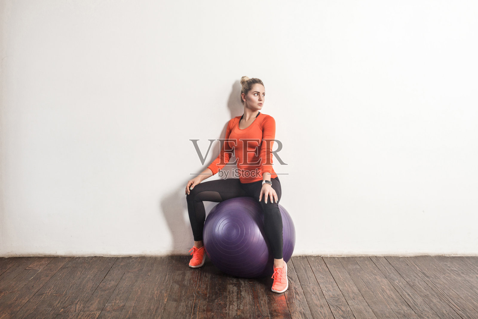 性感的金发女人坐在健身球靠近浅灰色的墙壁照片摄影图片