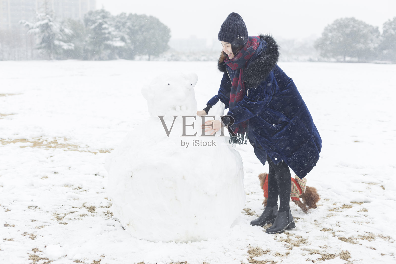 一个快乐的女人和她的狗在雪地上堆了一个大雪人照片摄影图片