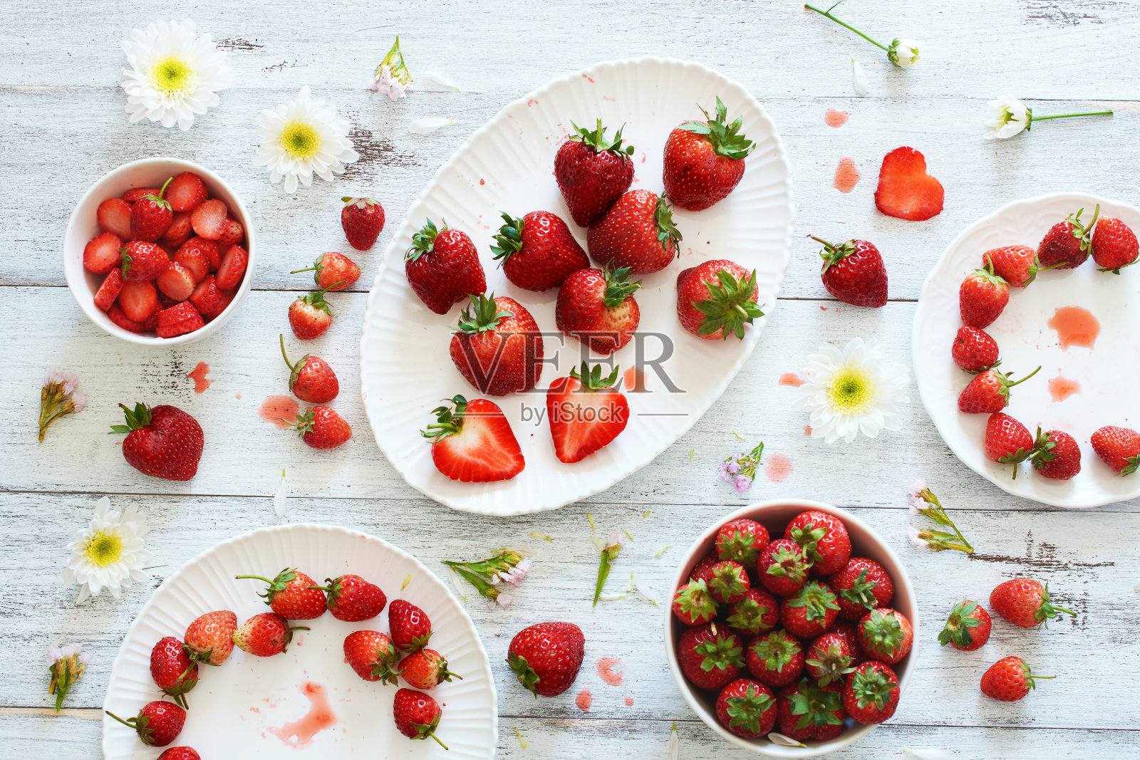 俯视图的新鲜草莓整个和切在碗和盘子装饰花在白色的桌子。照片摄影图片