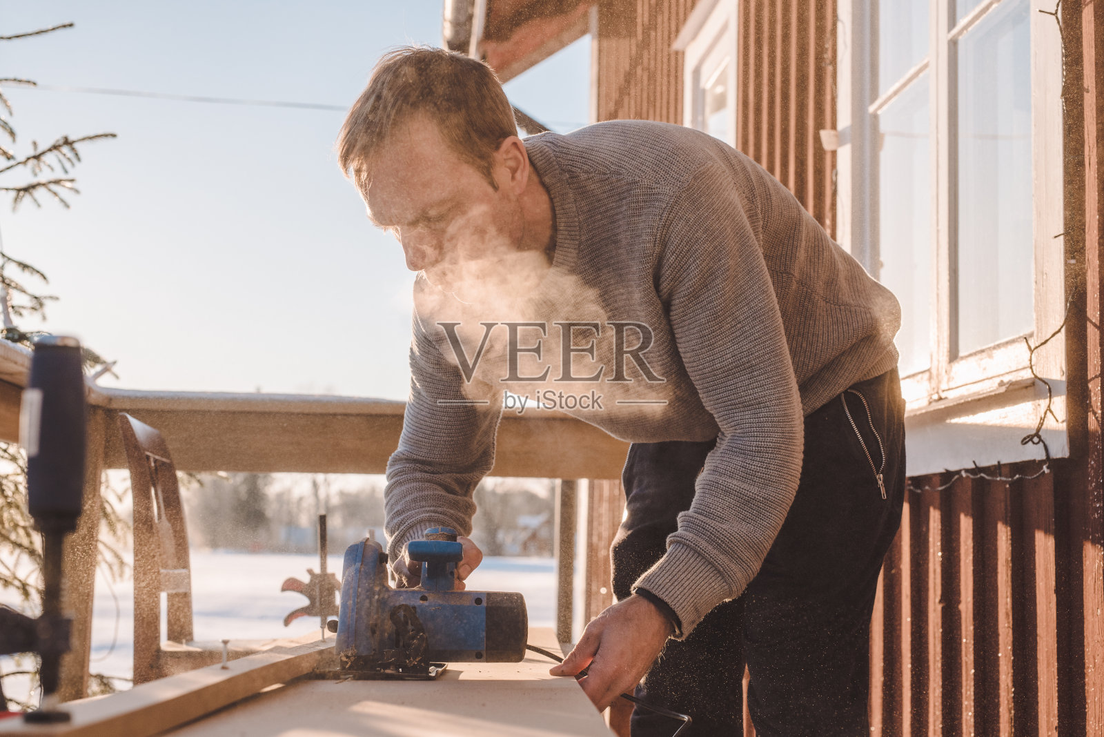 在寒冷的冬天，人们在室外锯木头，做木工照片摄影图片