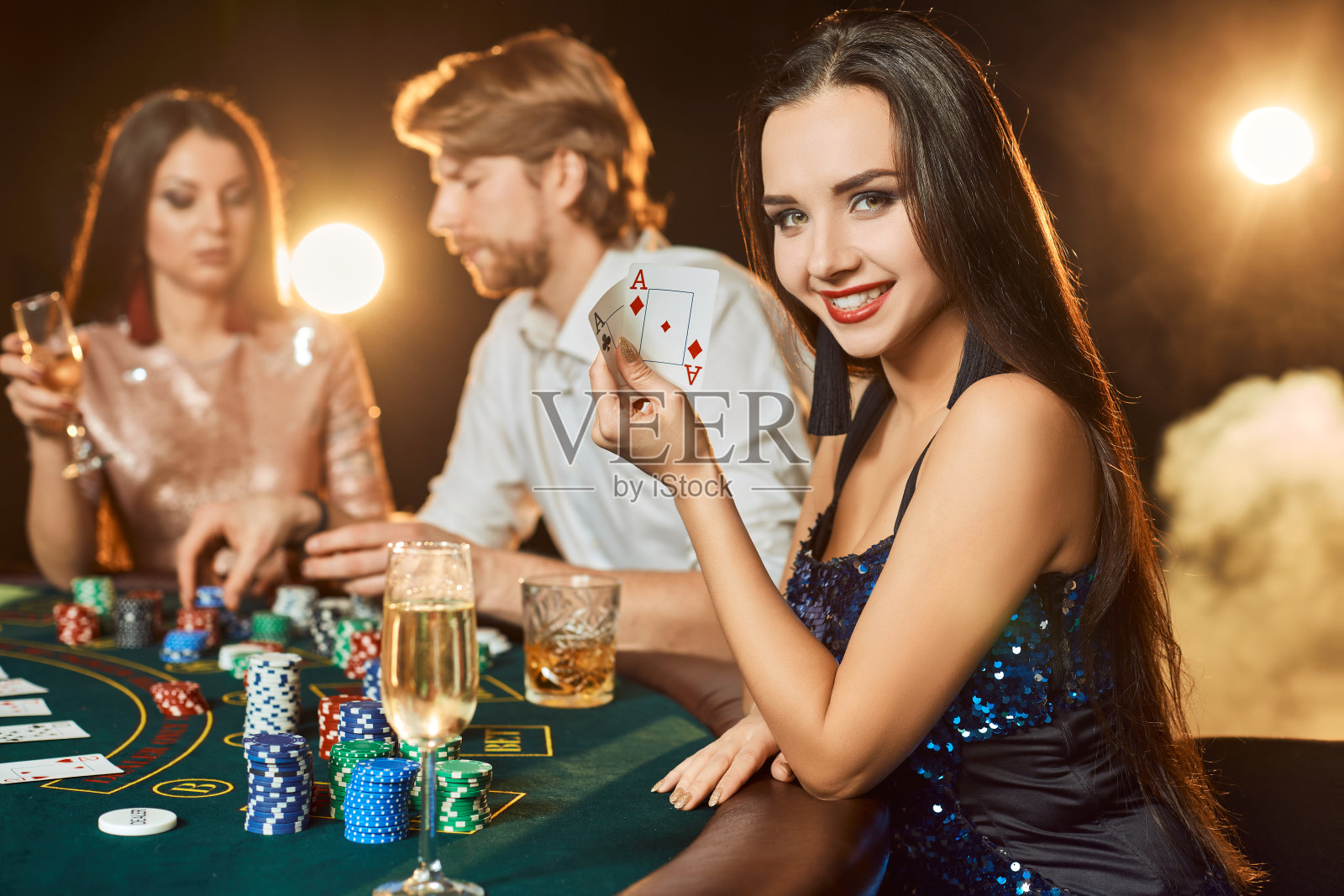 一群优雅的人在赌场玩扑克。关注一个穿着蓝色闪亮裙子的奢华的黑发女人照片摄影图片