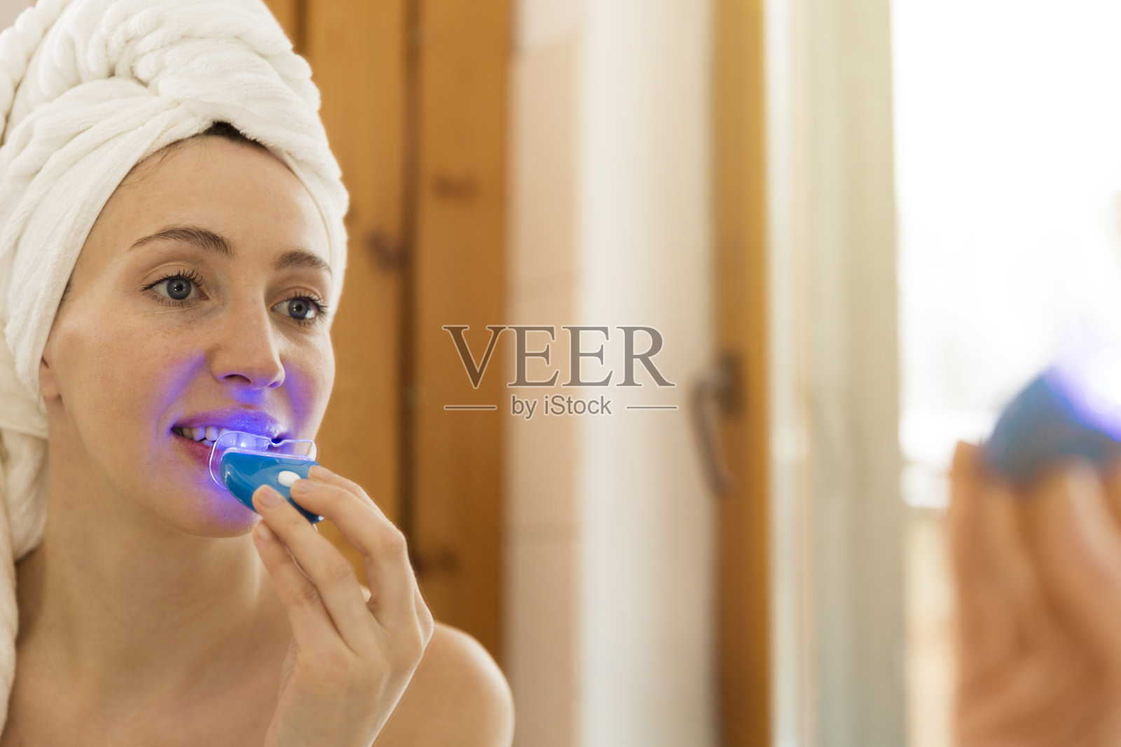 一个女人在家里用特殊的牙膏和LED灯美白牙齿。美丽的概念照片摄影图片