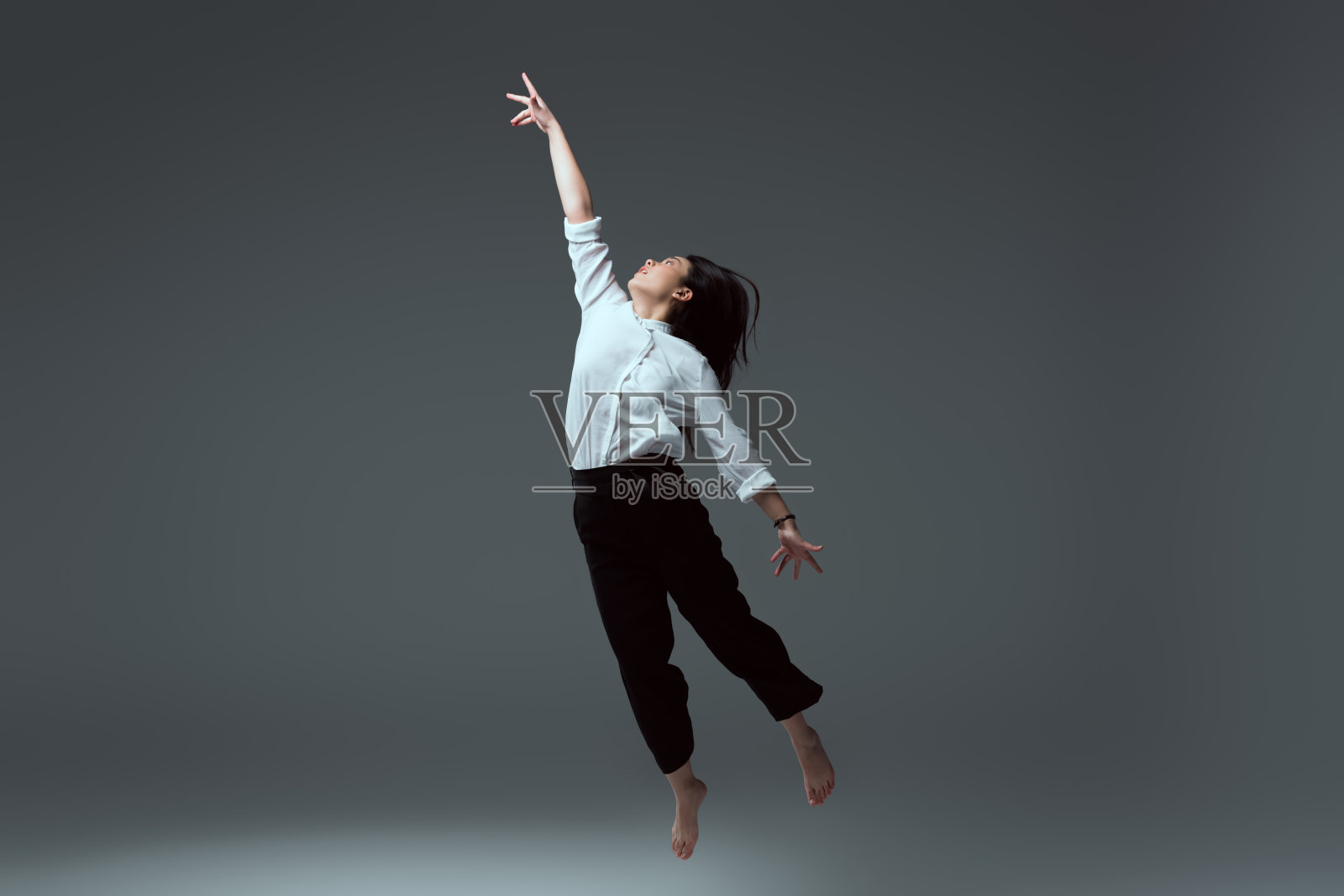 年轻的光着脚的女人在灰色上举起手跳跃照片摄影图片
