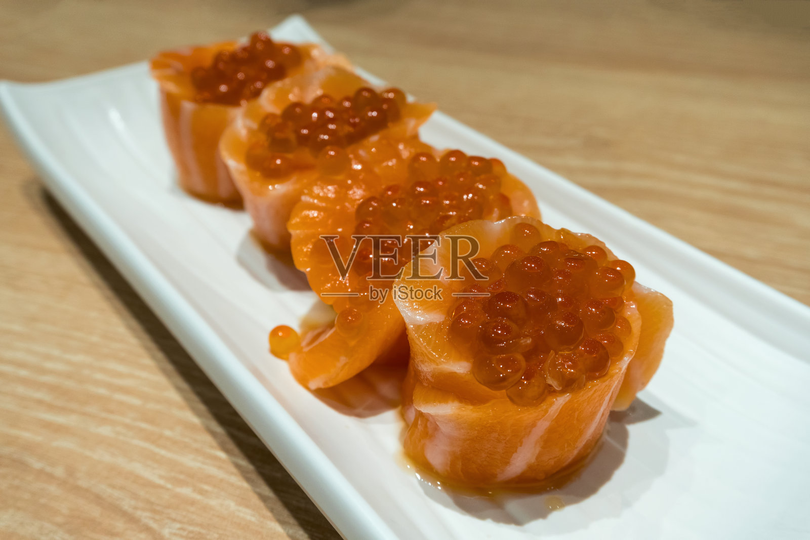 新鲜生鲑鱼寿司卷与鱼卵卵在长白色盘子特写宏照片摄影图片