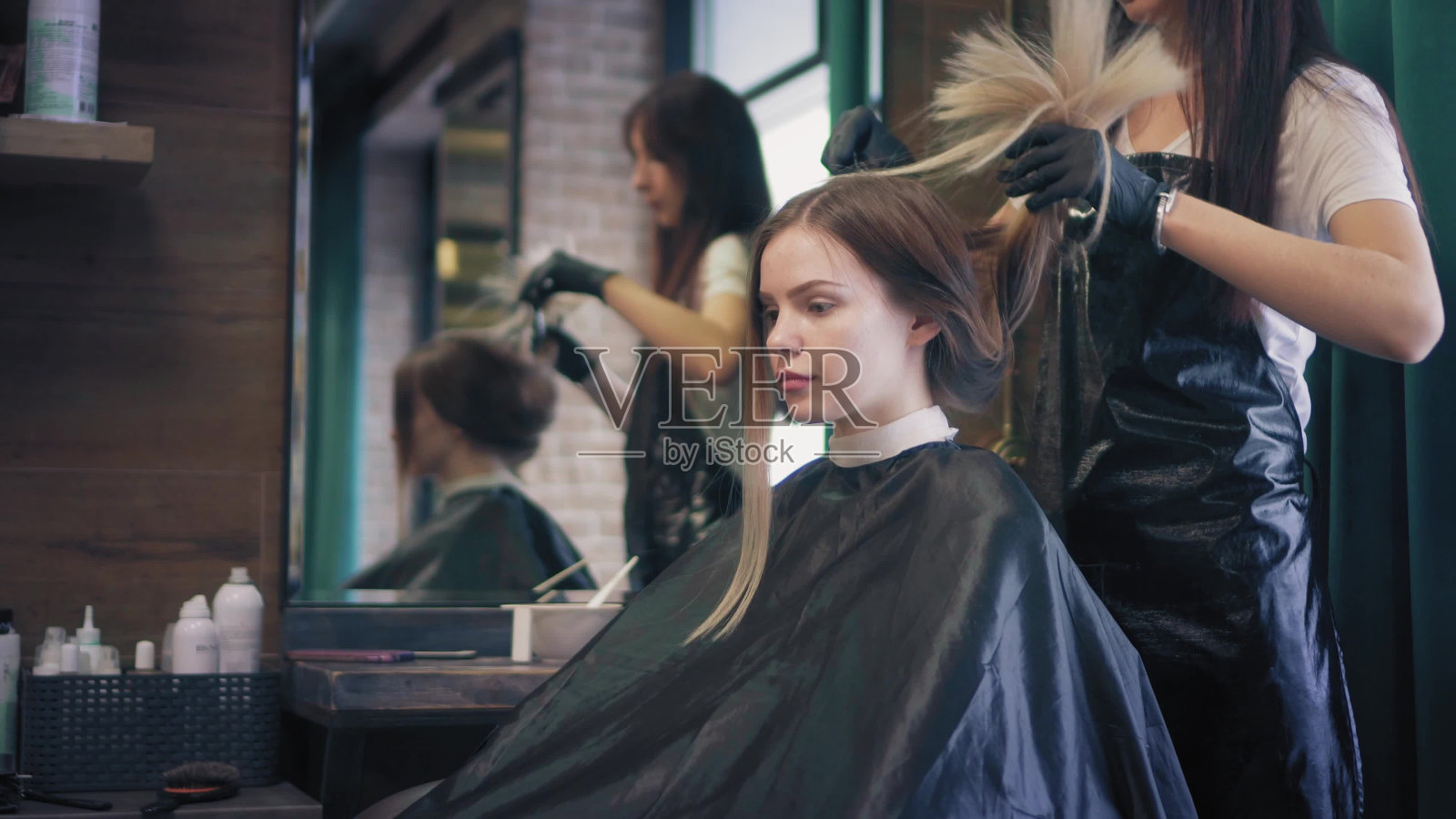 年轻的金发女郎坐在美容院的椅子上，美发师正在整理她的披肩，解开她的长发照片摄影图片