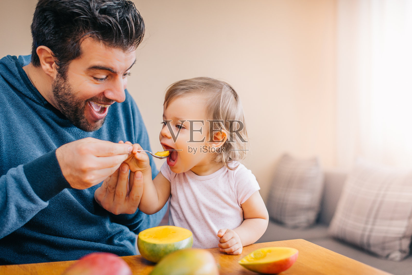 父亲用勺子和芒果喂蹒跚学步的婴儿照片摄影图片
