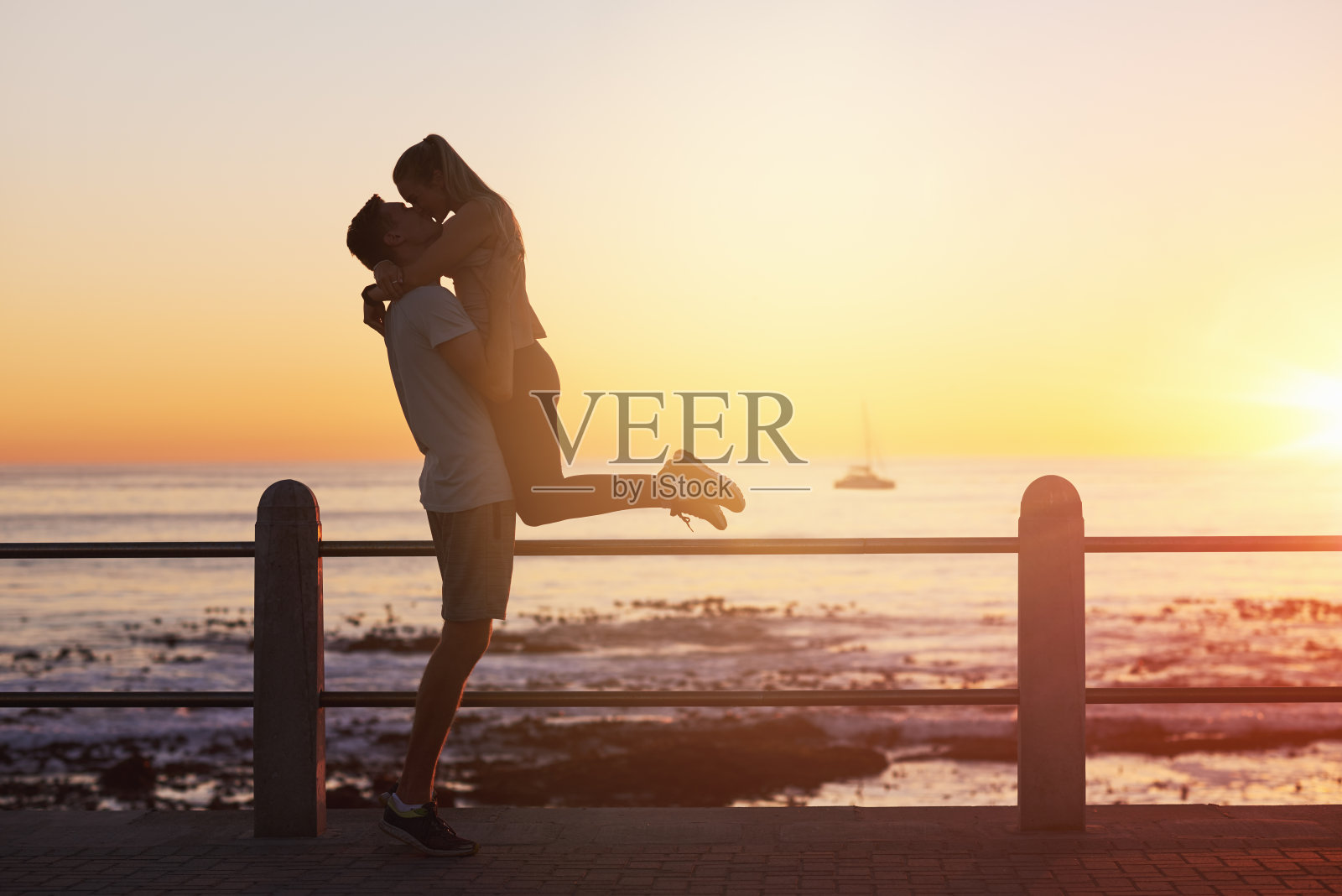 日落时分，年轻女子跳入男友的怀抱，给了他一个吻照片摄影图片