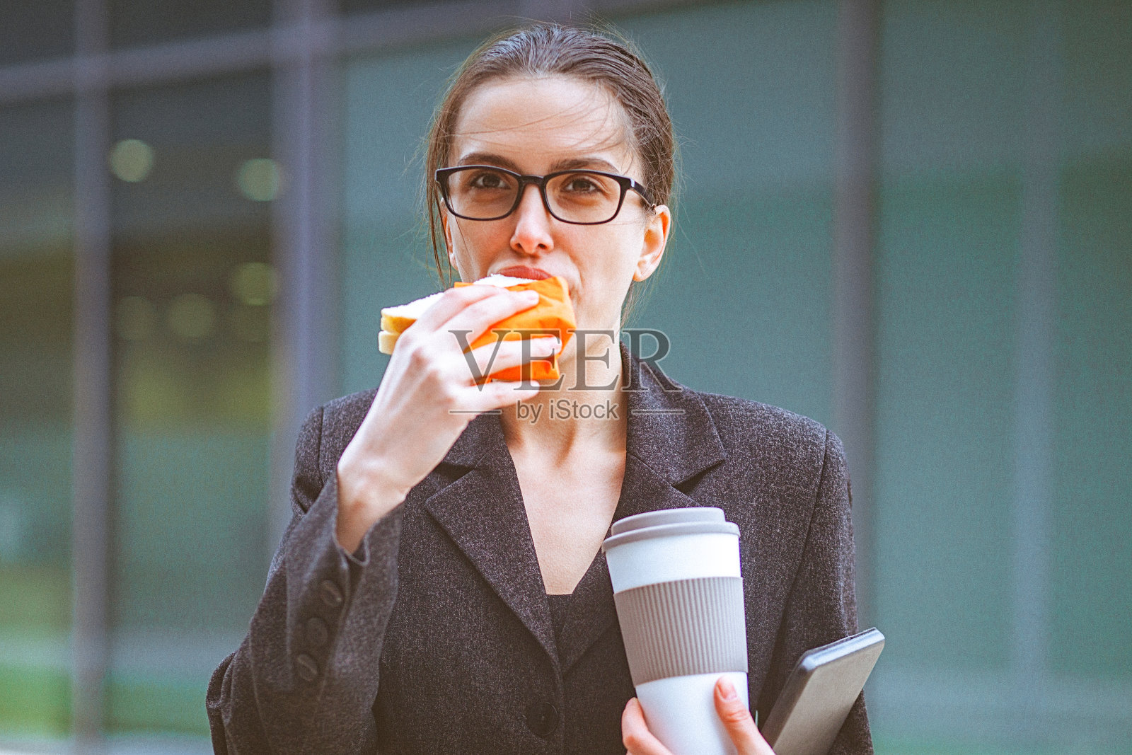 年轻的女商人在现代化的办公大楼前吃三明治照片摄影图片
