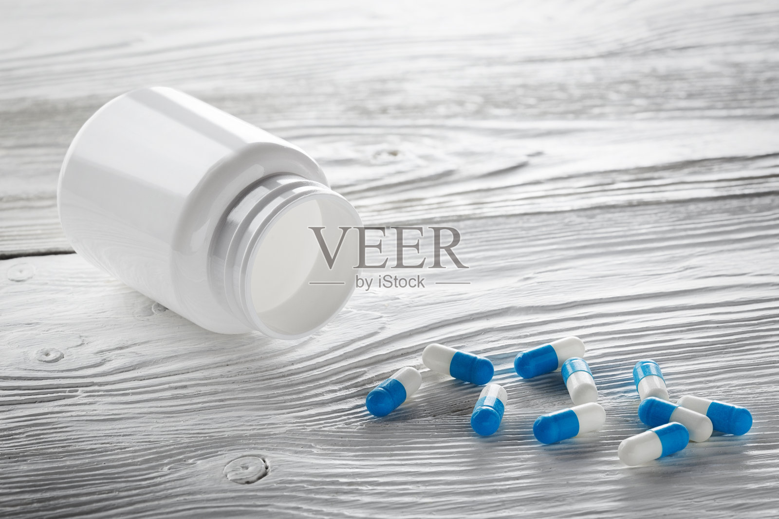 医用蓝色药丸和白色瓶子上的白色木制背景。照片摄影图片