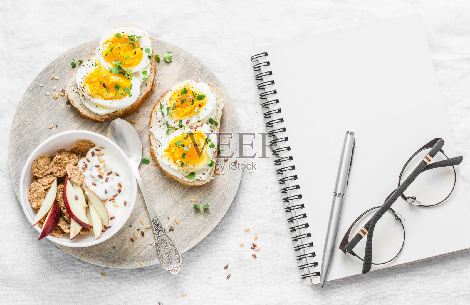 餐的饮食计划。健康的早餐或零食——三明治配软奶酪和煮鸡蛋，希腊酸奶配全麦谷物，亚麻籽，苹果和一个干净的空白笔记本在一个明亮的背景，俯视图。平躺照片摄影图片