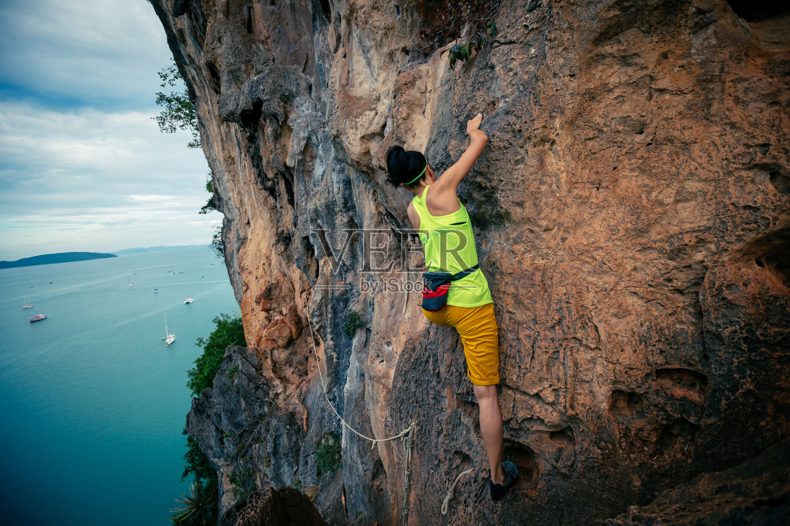 女攀岩者在海边陡峭的悬崖上攀岩照片摄影图片