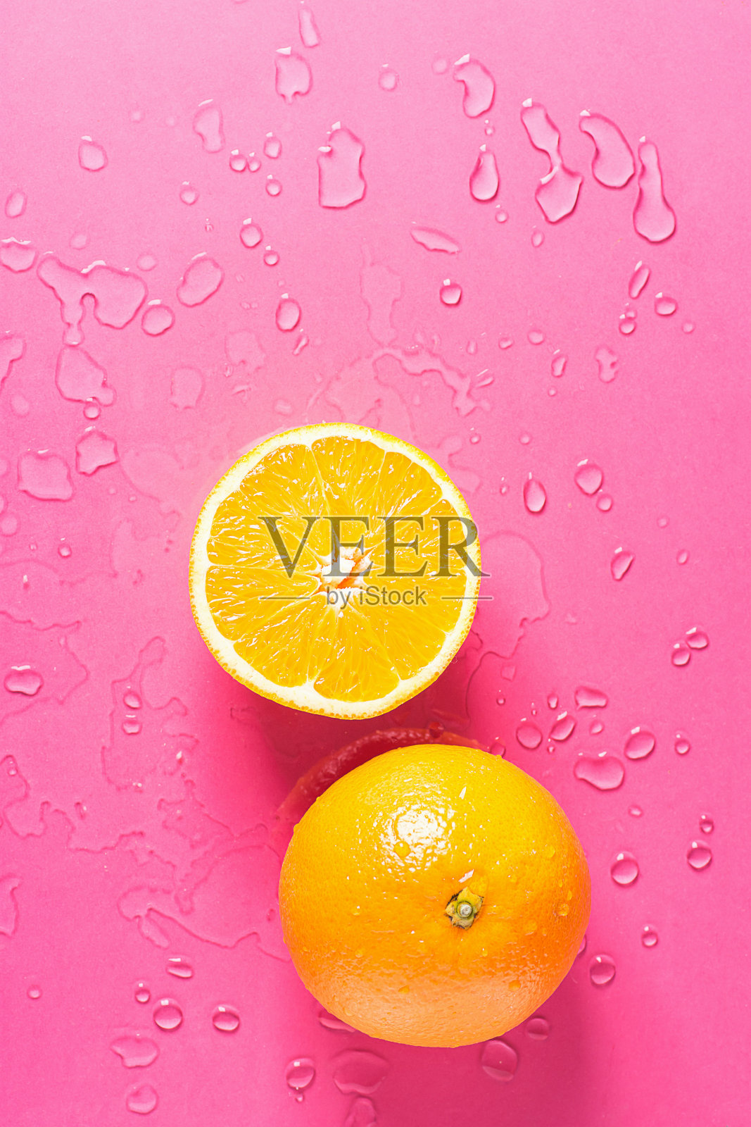 成熟多汁的整个和减半的橙子，桃红色背景和水滴。维生素健康饮食夏季排毒素食超级食物概念。海报横幅模板。复制空间平面铺设照片摄影图片
