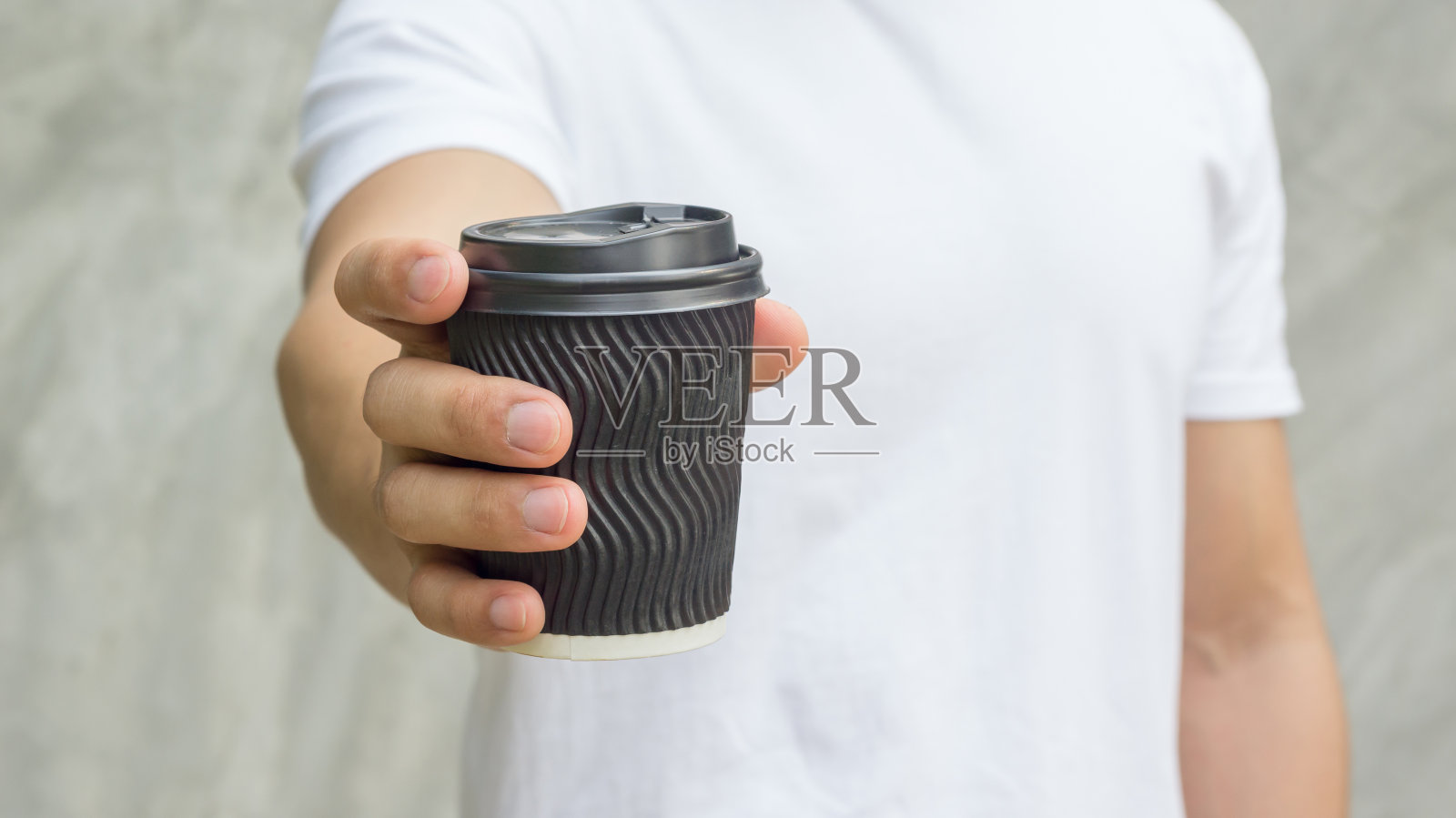 灰色背景下，拿着一杯咖啡的男人。照片摄影图片