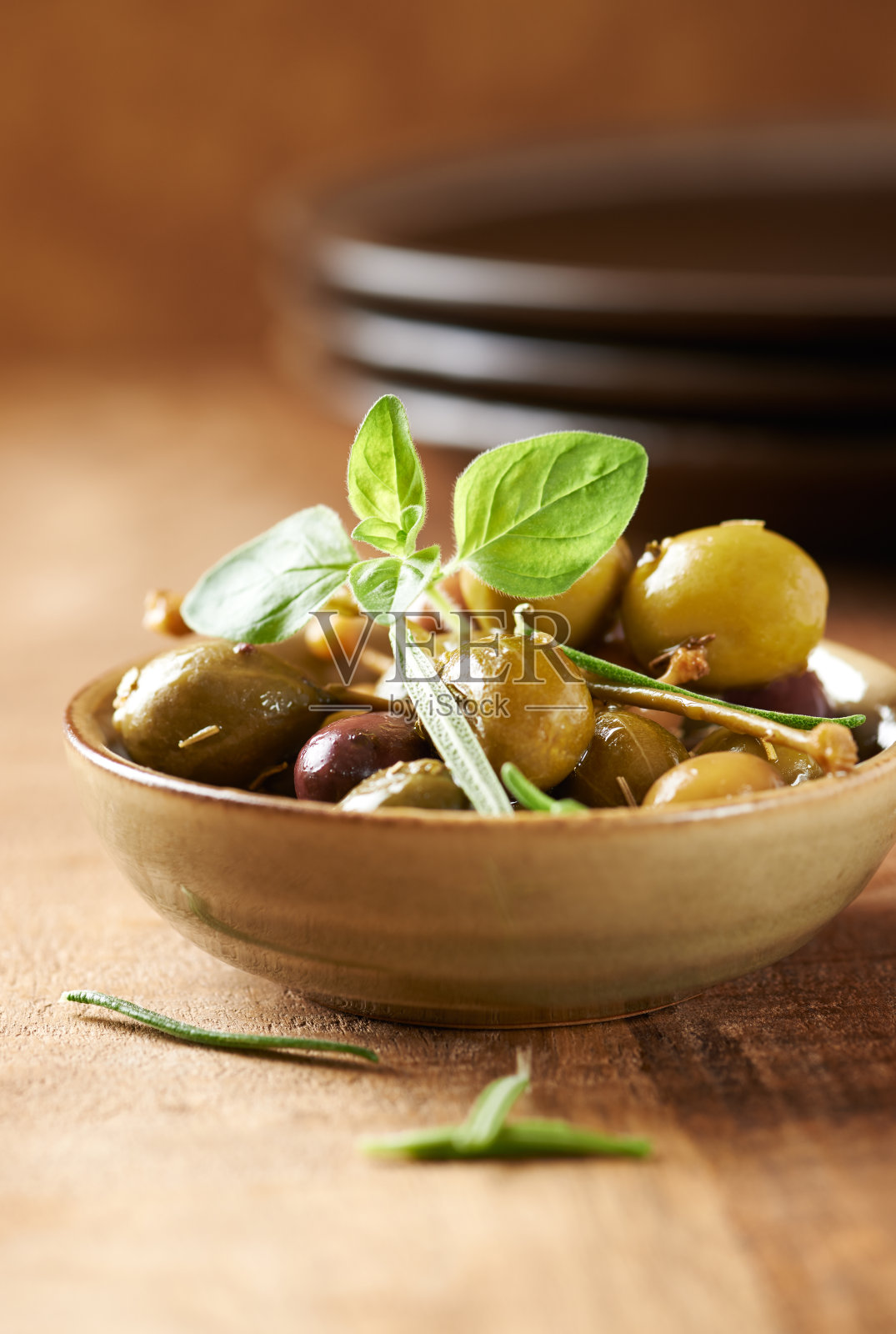 不同腌制过的橄榄和刺山柑放在一个小陶瓷碗里。垂直的。照片摄影图片