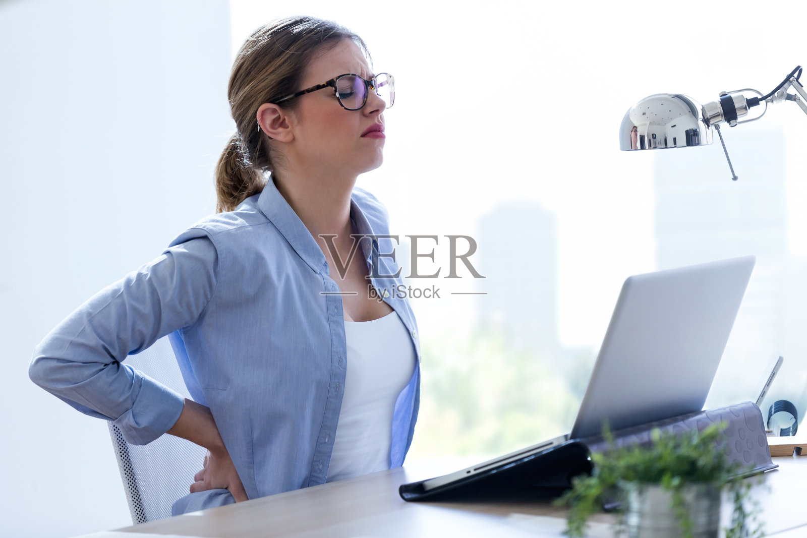 疲惫的年轻女子背部疼痛使用她的笔记本电脑在家里。照片摄影图片