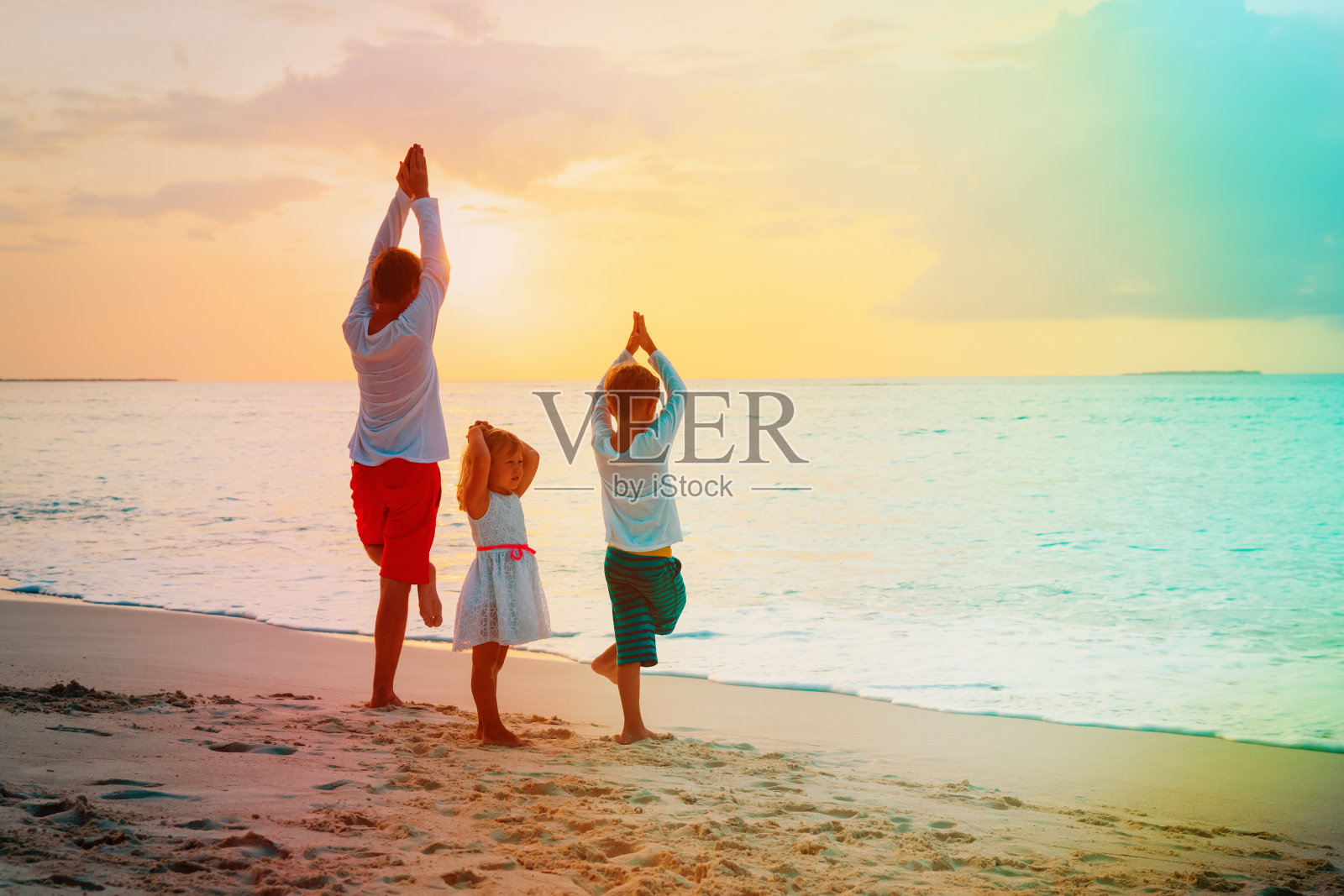父亲和儿子和女儿在日落海滩做瑜伽照片摄影图片
