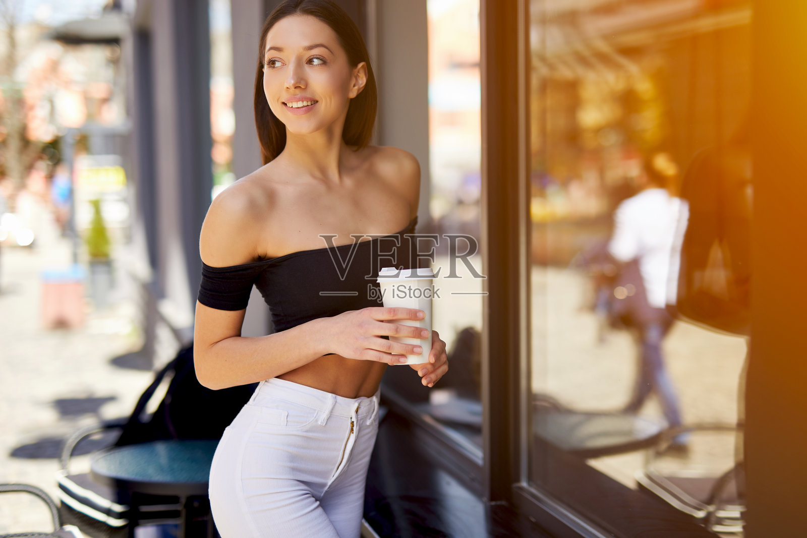 黑发女孩站在街上看着镜头，喝着白色杯子里的美味咖啡，拍摄春天的照片照片摄影图片
