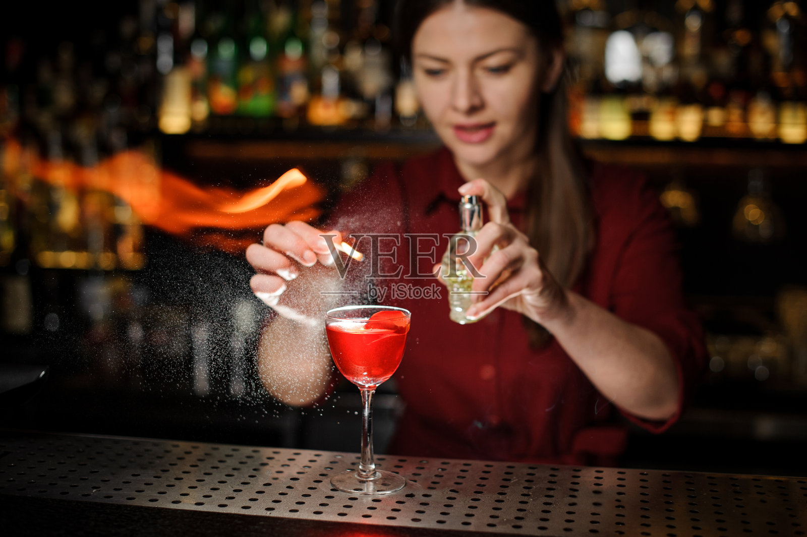 酒保女孩把泥炭威士忌加到含酒精的鸡尾酒里，然后喷在玻璃杯上的火上照片摄影图片