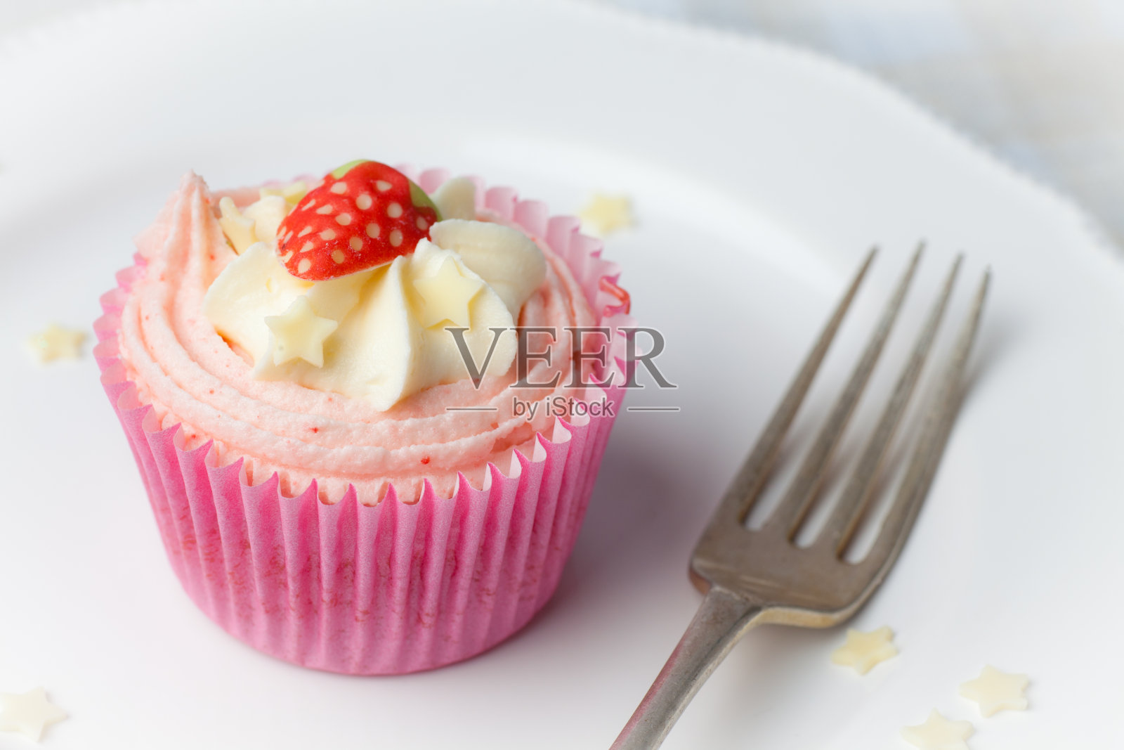 白色盘子上有星星点缀的粉色草莓纸杯蛋糕照片摄影图片