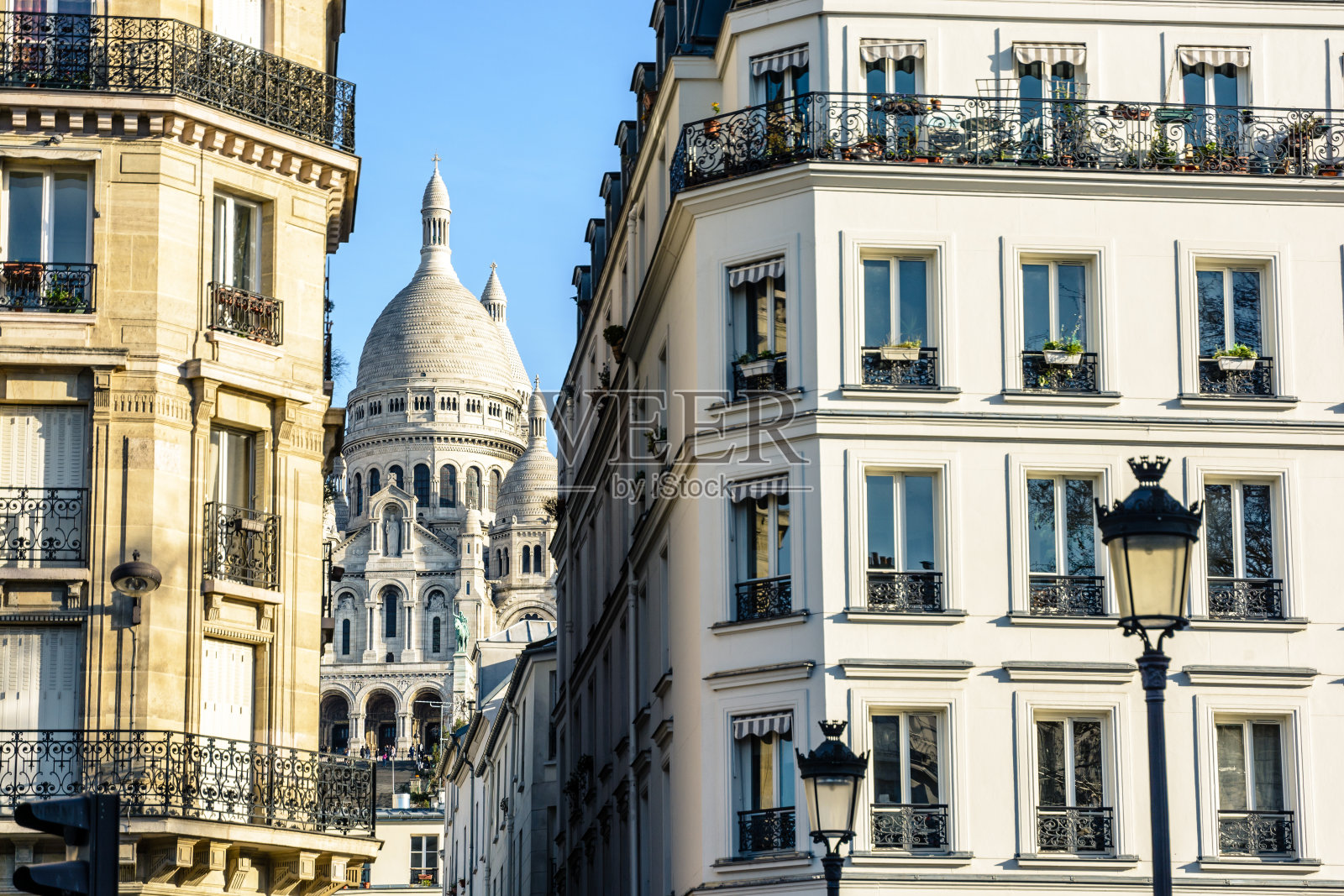 在清澈的蓝天下，通过一条狭窄的街道，可以看到巴黎圣心大教堂的正面和圆顶。照片摄影图片