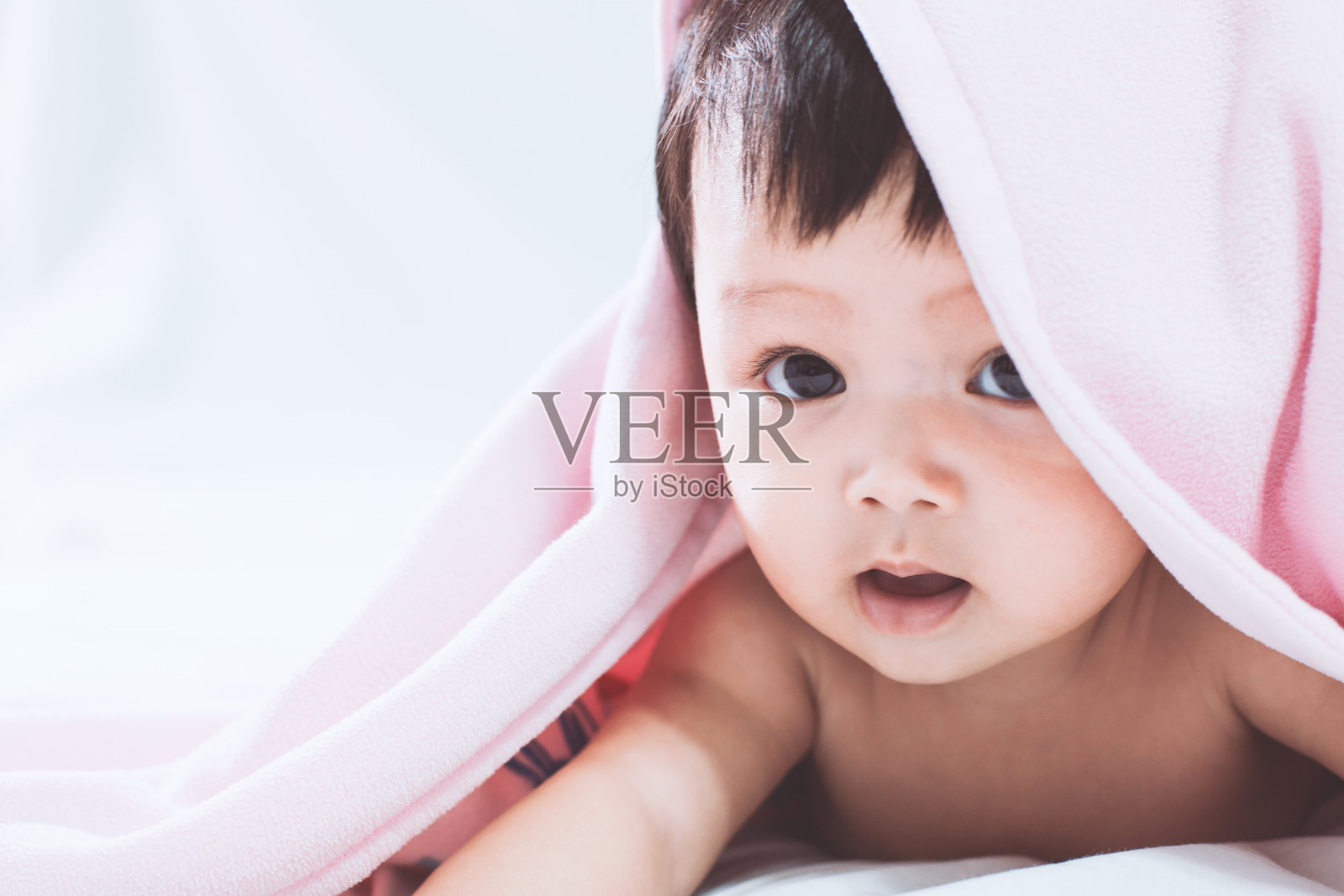 可爱的亚洲小女孩在粉红色的毯子下微笑，腹部躺在床上照片摄影图片