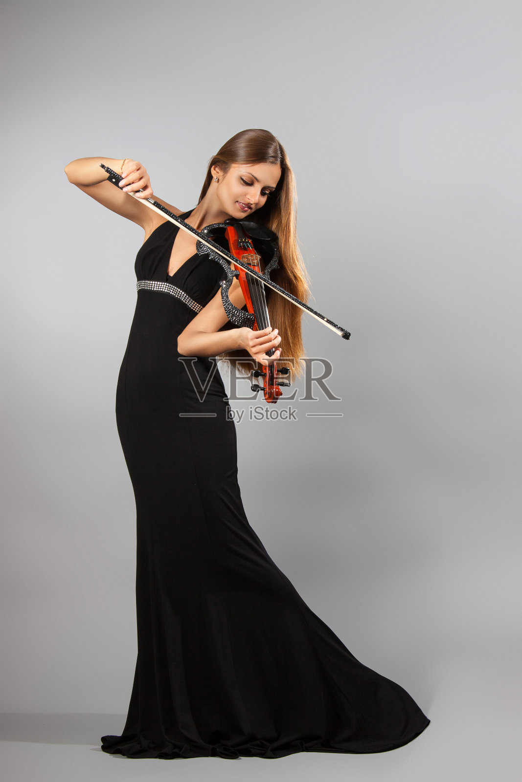女孩在灰色的背景上拉着小提琴。她拉小提琴照片摄影图片