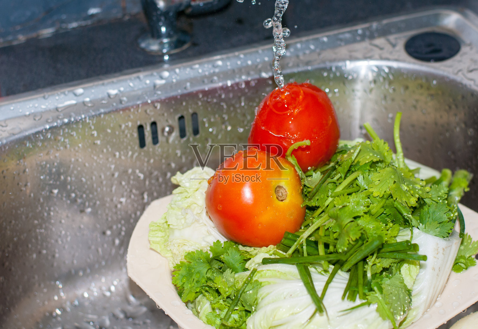 两个鲜红的西红柿和绿色的西芹正在清洗，水从厨房的银水槽上落下，准备食物配料照片摄影图片