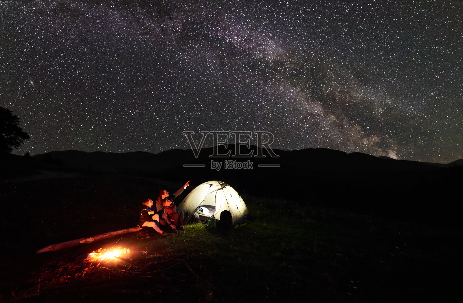 父亲和两个孩子在山间露营休息在星空和银河下照片摄影图片