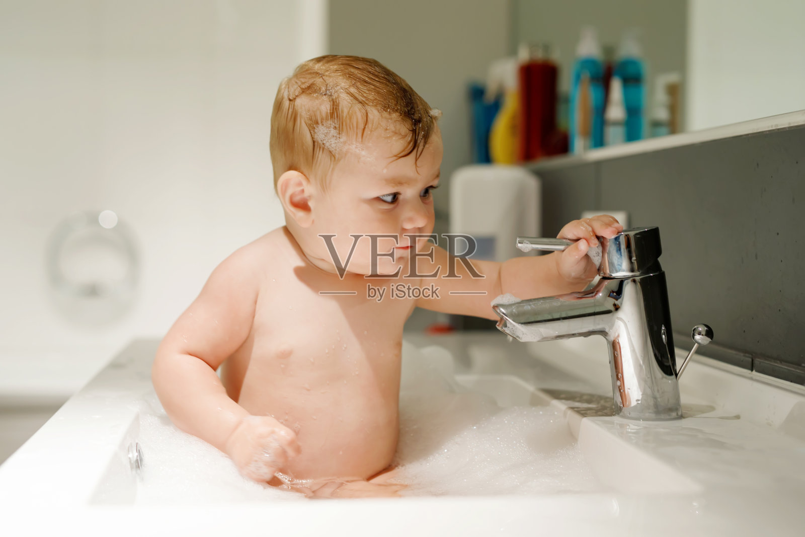 可爱可爱的宝宝在洗脸盆里洗澡，玩水和泡沫照片摄影图片