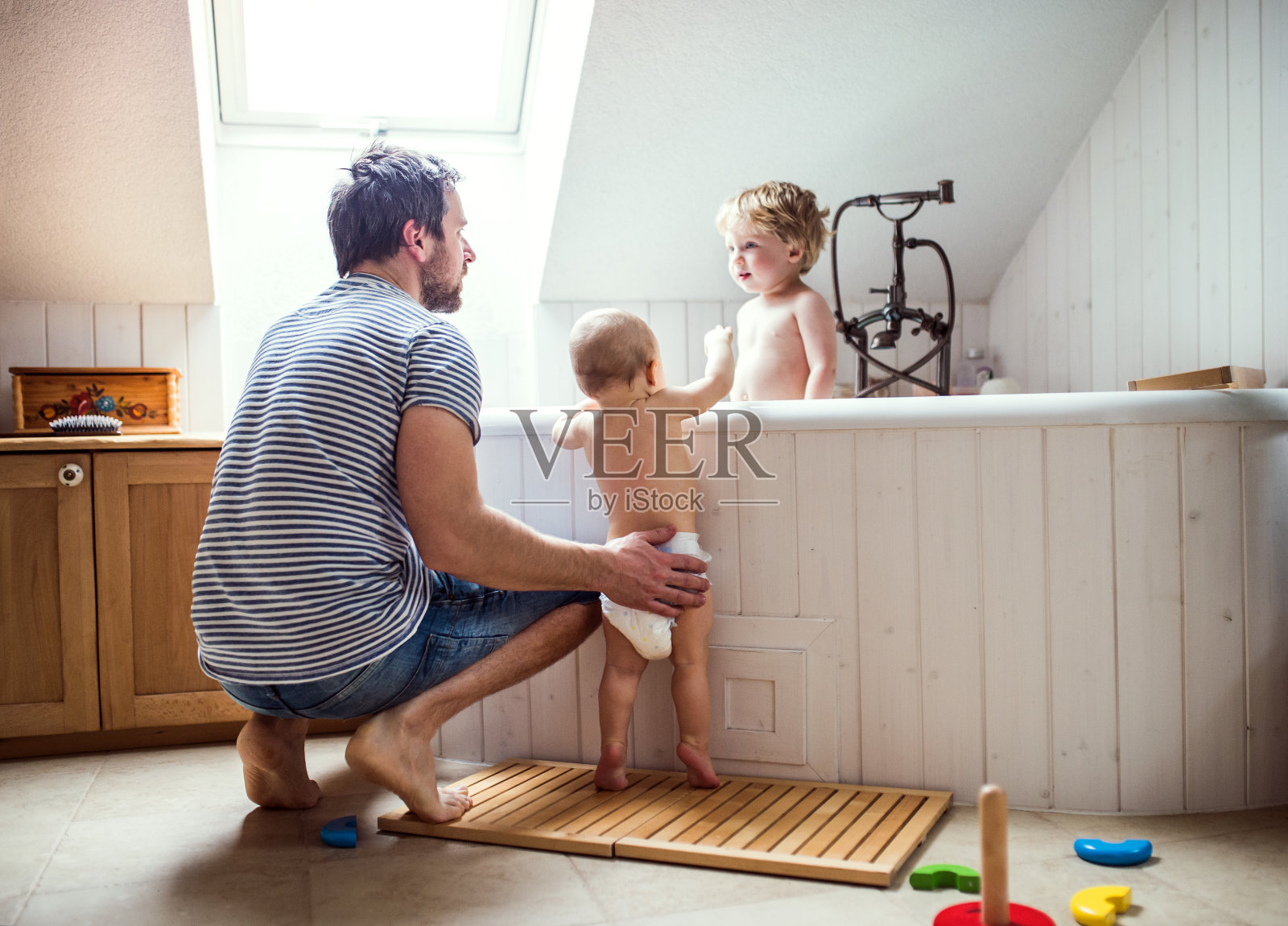 父亲在家里的浴室里给两个蹒跚学步的孩子洗澡。照片摄影图片