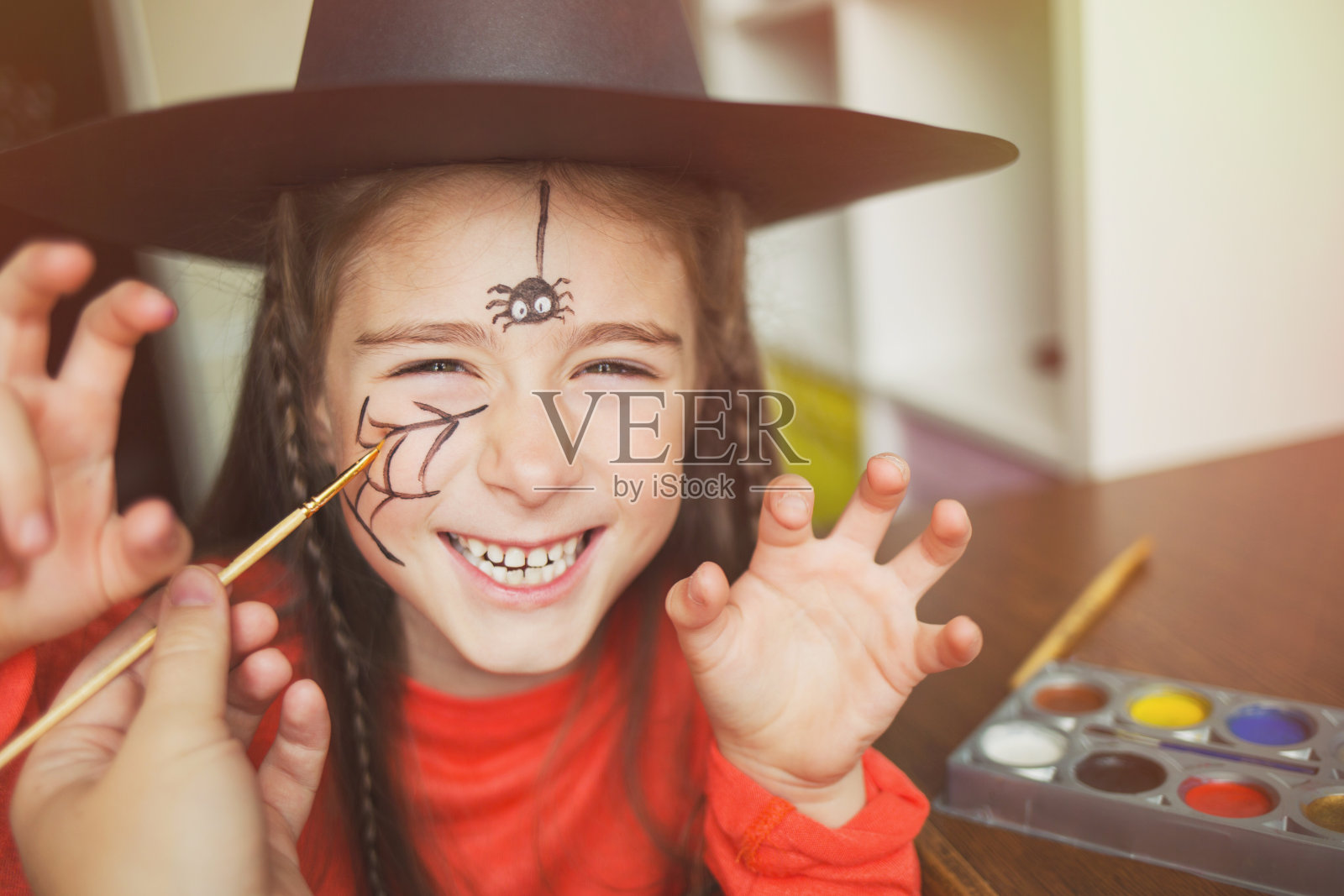 为万圣节做准备。穿着女巫服的孩子在做脸部彩绘。可爱的蜘蛛。简单套装的理念，diy照片摄影图片