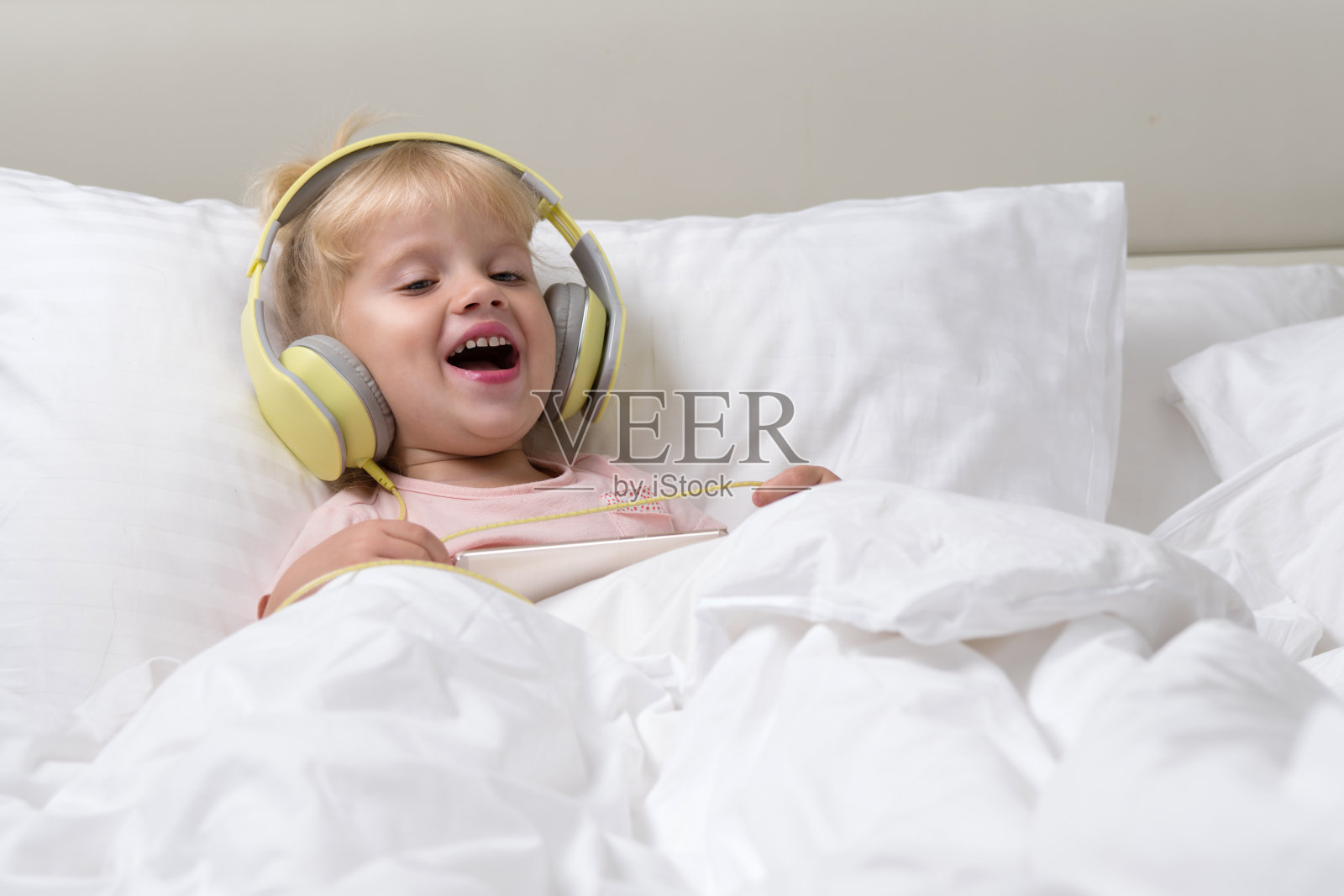 小宝贝小女孩躺在白色的床上戴着耳机用手机听着音乐开心的笑着开心的早晨照片摄影图片