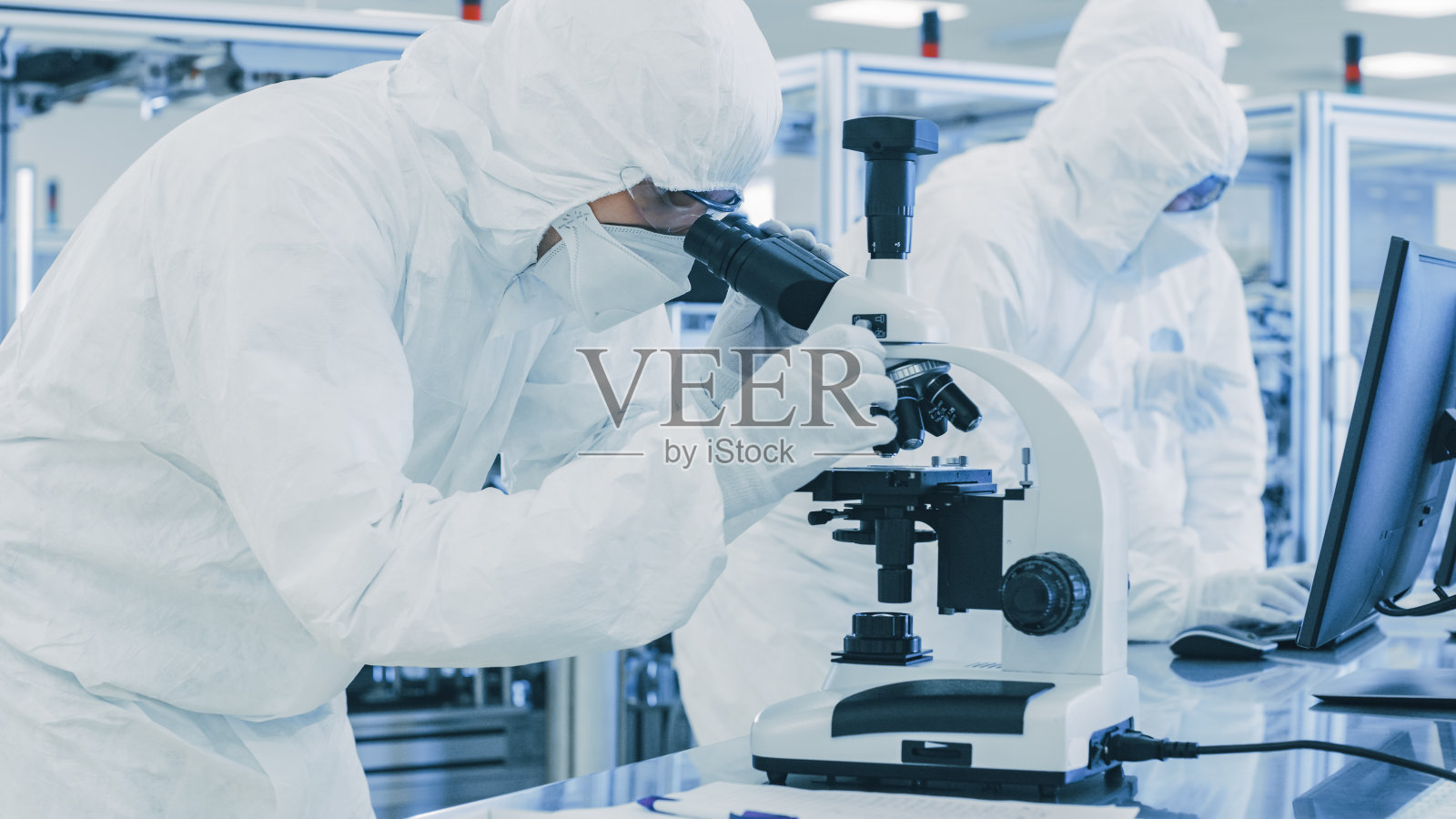 在实验室科学家穿着防护服做研究，使用显微镜和记录数据。工人在一个现代制造生产半导体和药品。照片摄影图片
