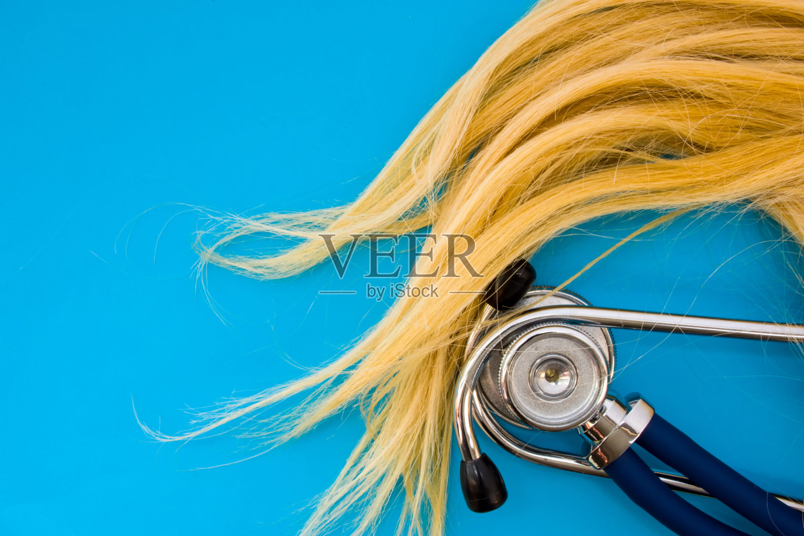 金色卷发和蓝色背景上的听诊器占据了照片的一半，下半部分空白的地方是标题。概念照片的医疗和美容美发护理，疾病的治疗照片摄影图片