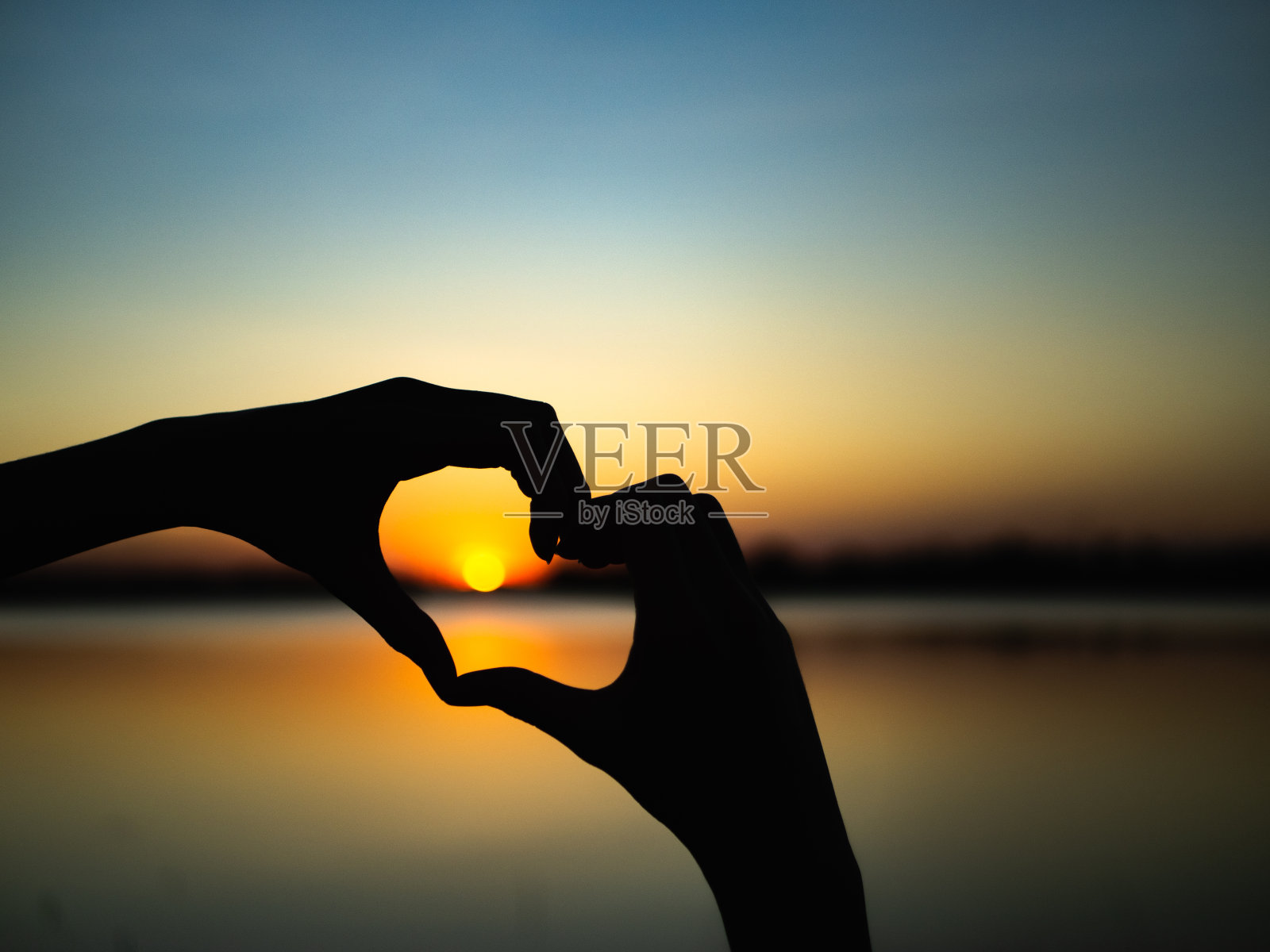 在夕阳的背景上，手的剪影是心的形状。快乐，爱情，情人节的概念，标志，象征，概念。照片摄影图片