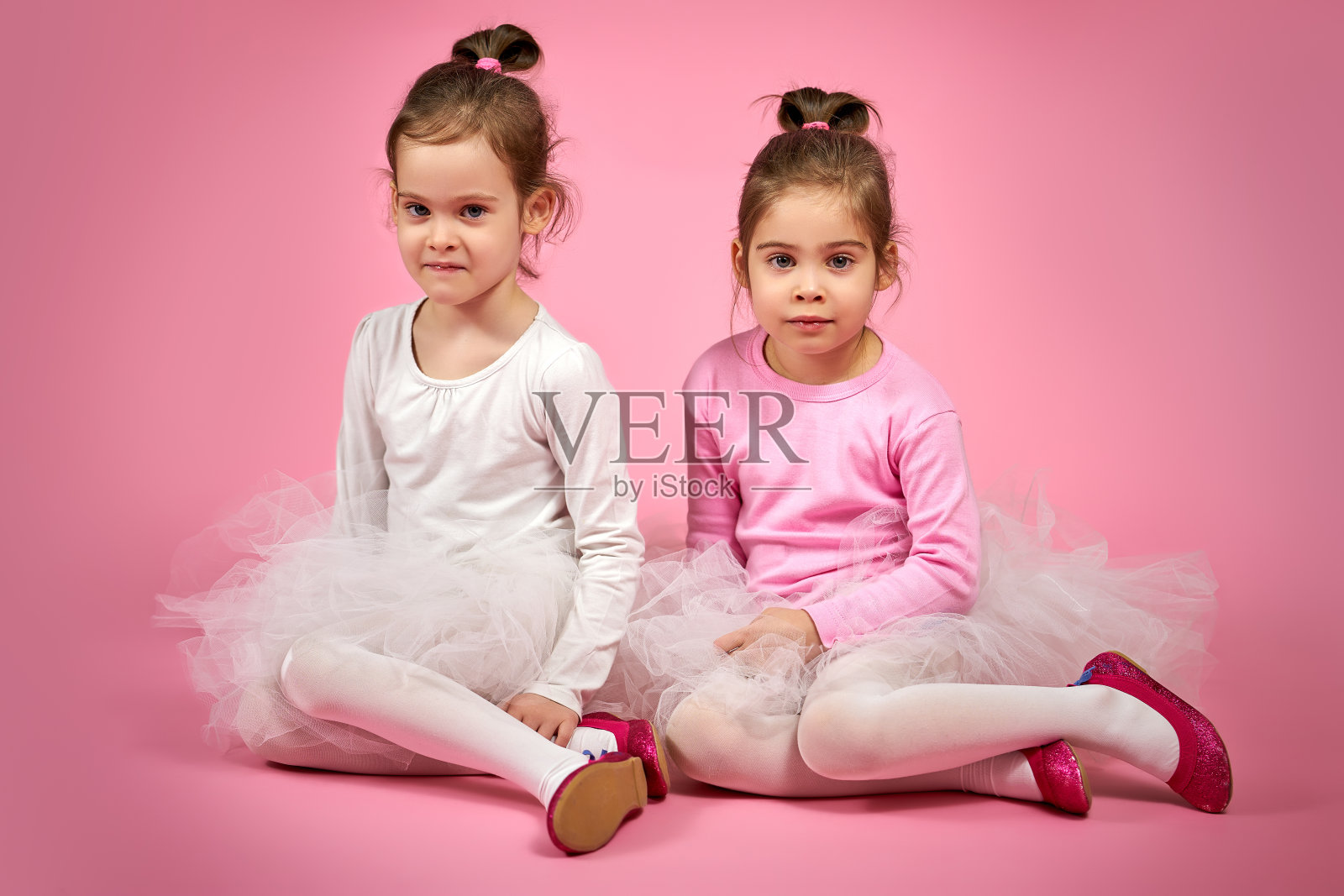 两个可爱的小女孩穿着薄纱裙，粉红色的背景照片摄影图片