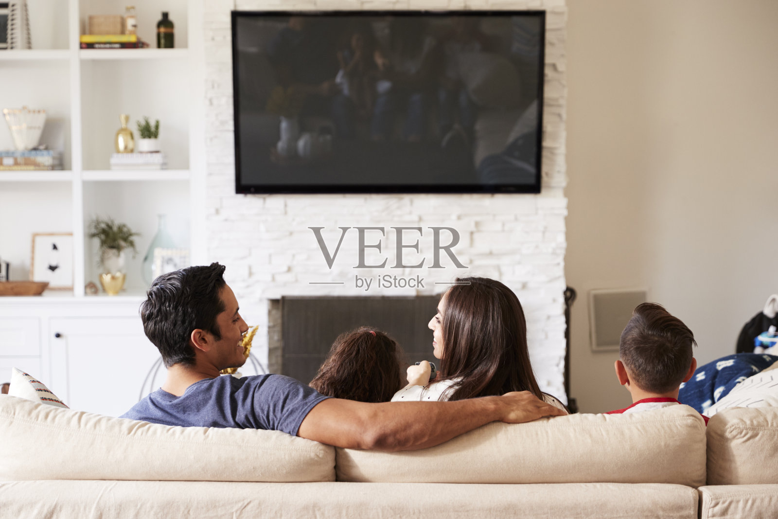 一个年轻的西班牙家庭四人坐在沙发上看电视，妈妈看着爸爸照片摄影图片