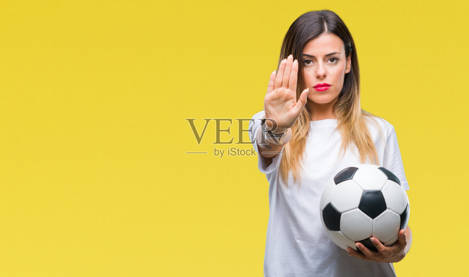 年轻美丽的女人拿着足球在孤立的背景与开放的手做停止标志与严肃和自信的表情，防御手势照片摄影图片