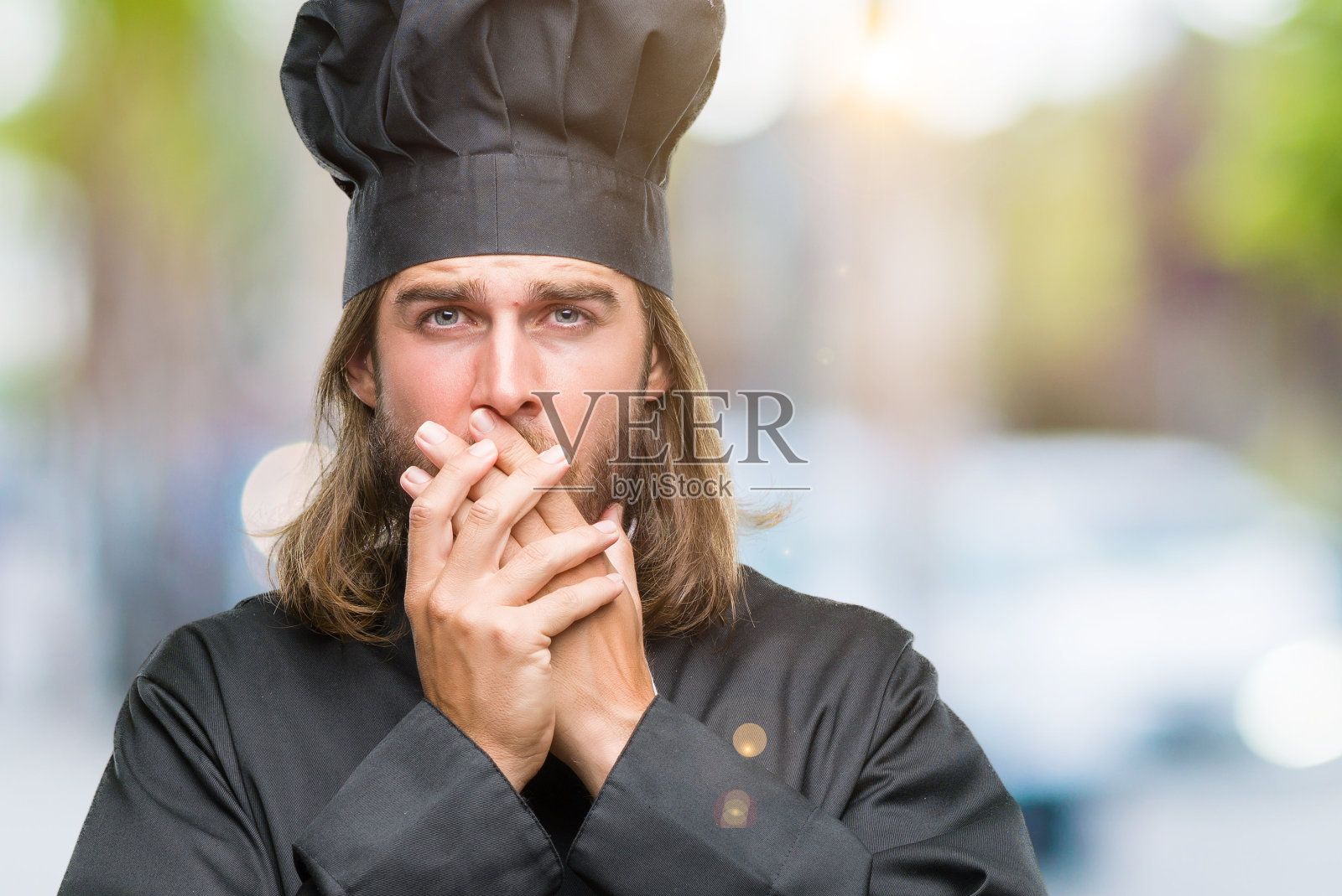 年轻英俊的厨师与长头发在孤立的背景震惊掩盖嘴与手为错误。秘密的概念。照片摄影图片