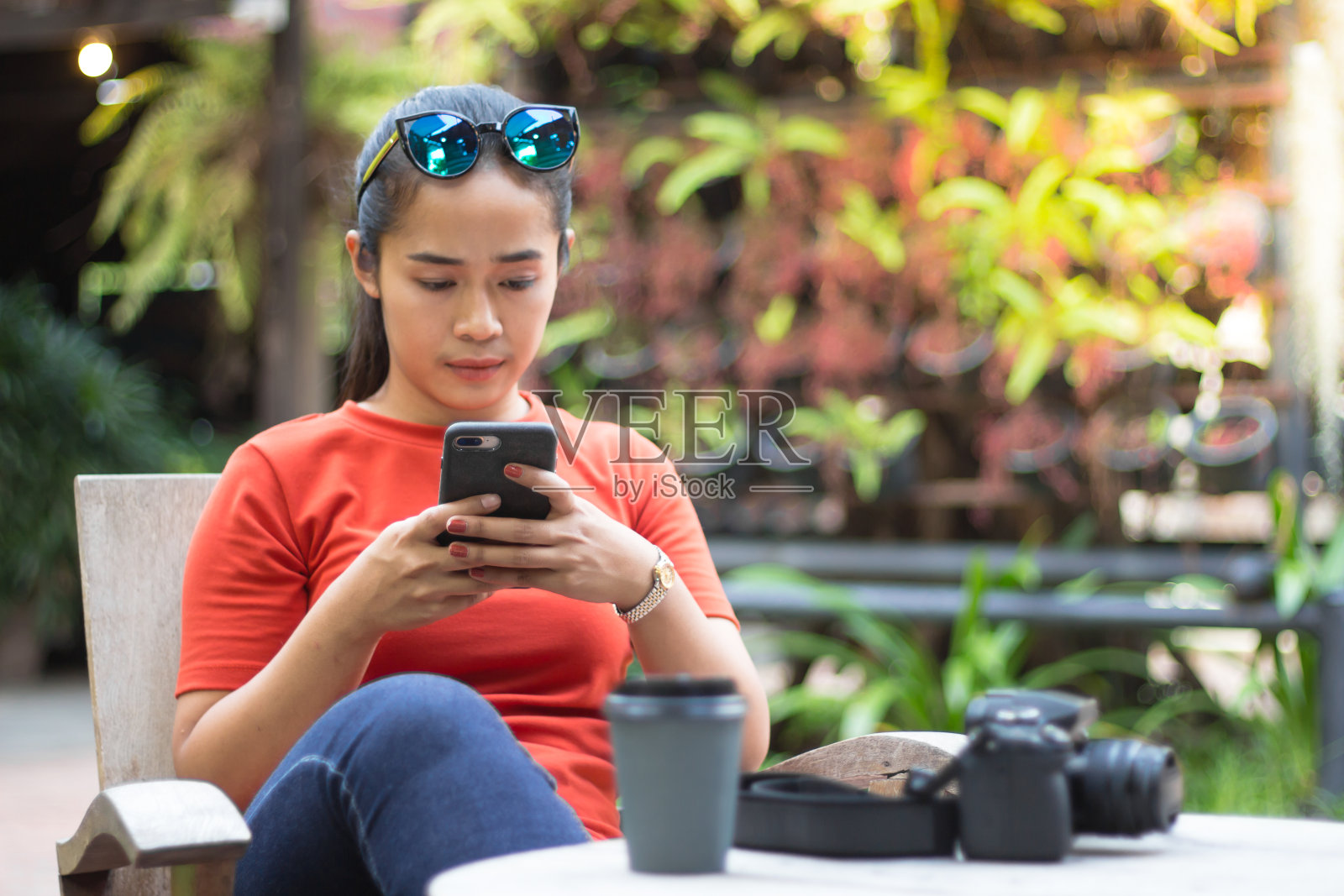 女人正在用手机上网，有一个摄像头，一个咖啡杯在木桌上。照片摄影图片