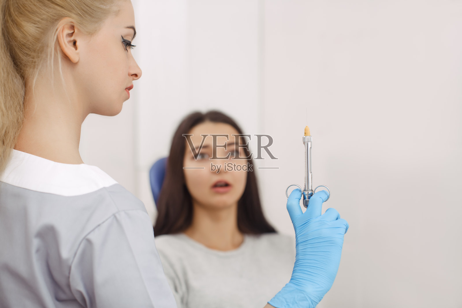 牙医拿着注射器，惊恐的病人在后面照片摄影图片